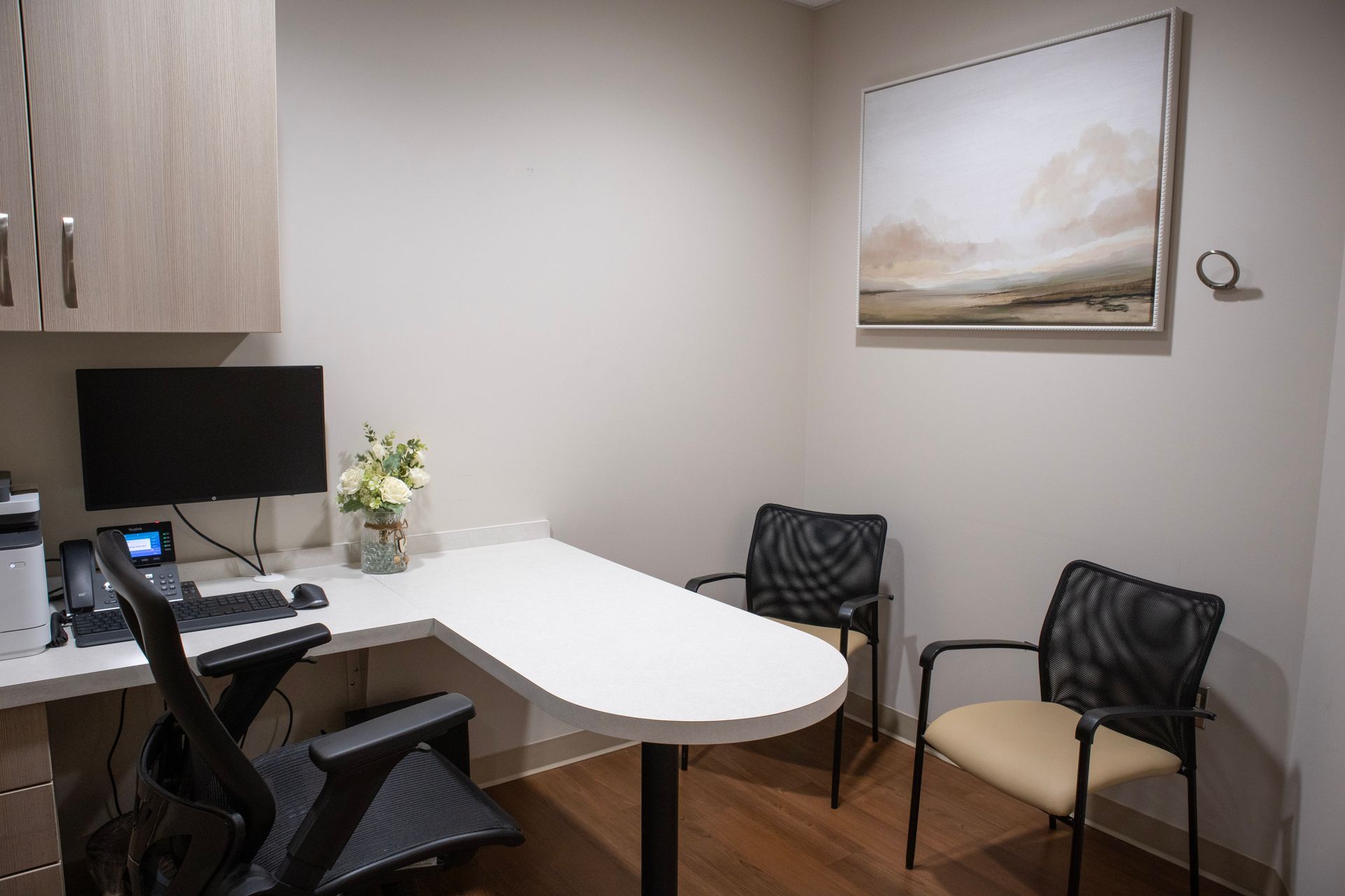 Small office with a white desk, computer, black chairs, and framed wall art.