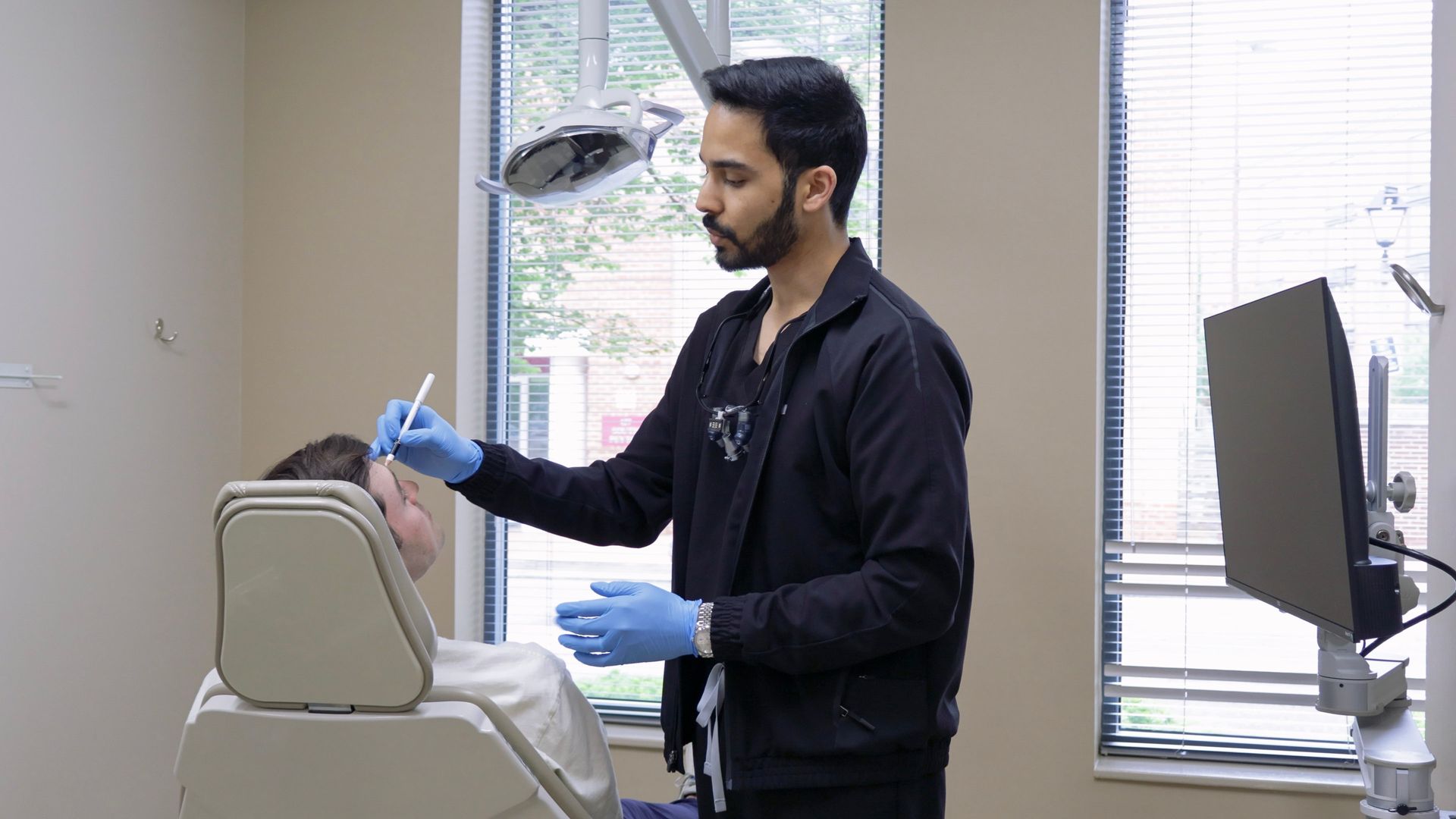 Person receiving a facial injection. A gloved hand holds a syringe near the brow, in a clinical setting.