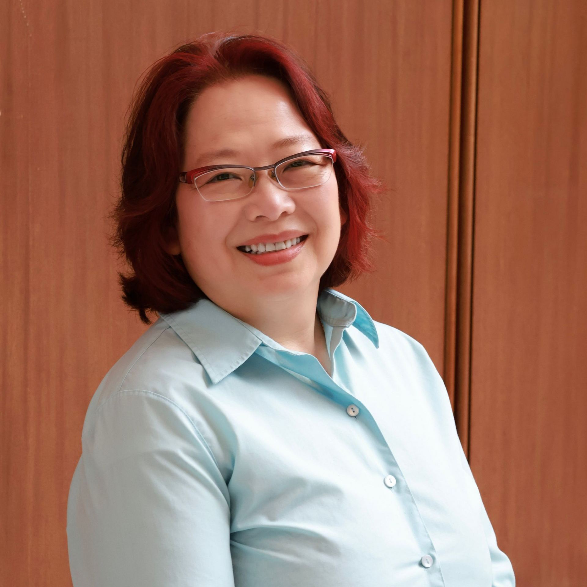 Woman smiling, wearing a white lab coat with a light blue collared shirt.