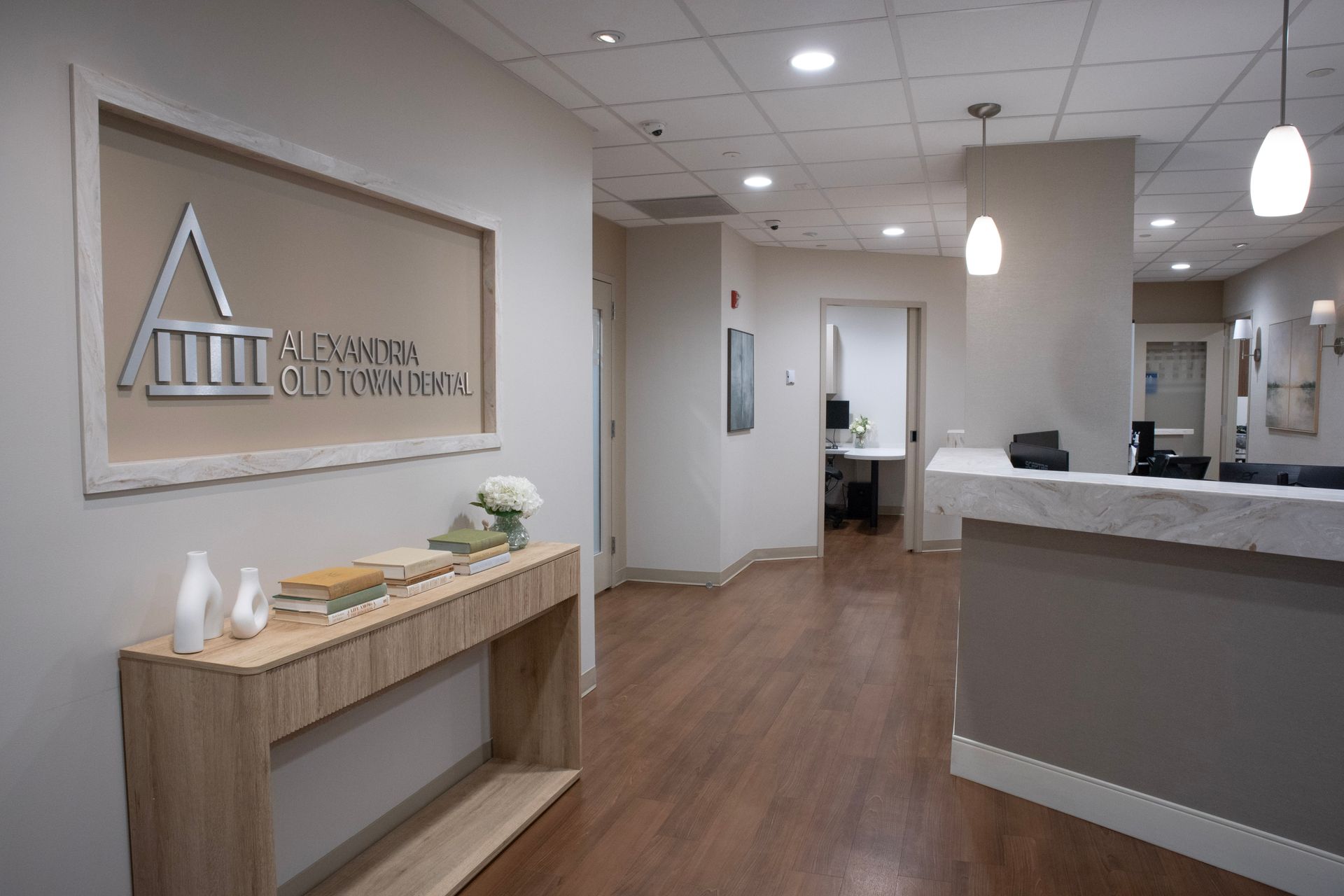 Bright modern clinic lobby with reception desk, wood floor, and wall logo.