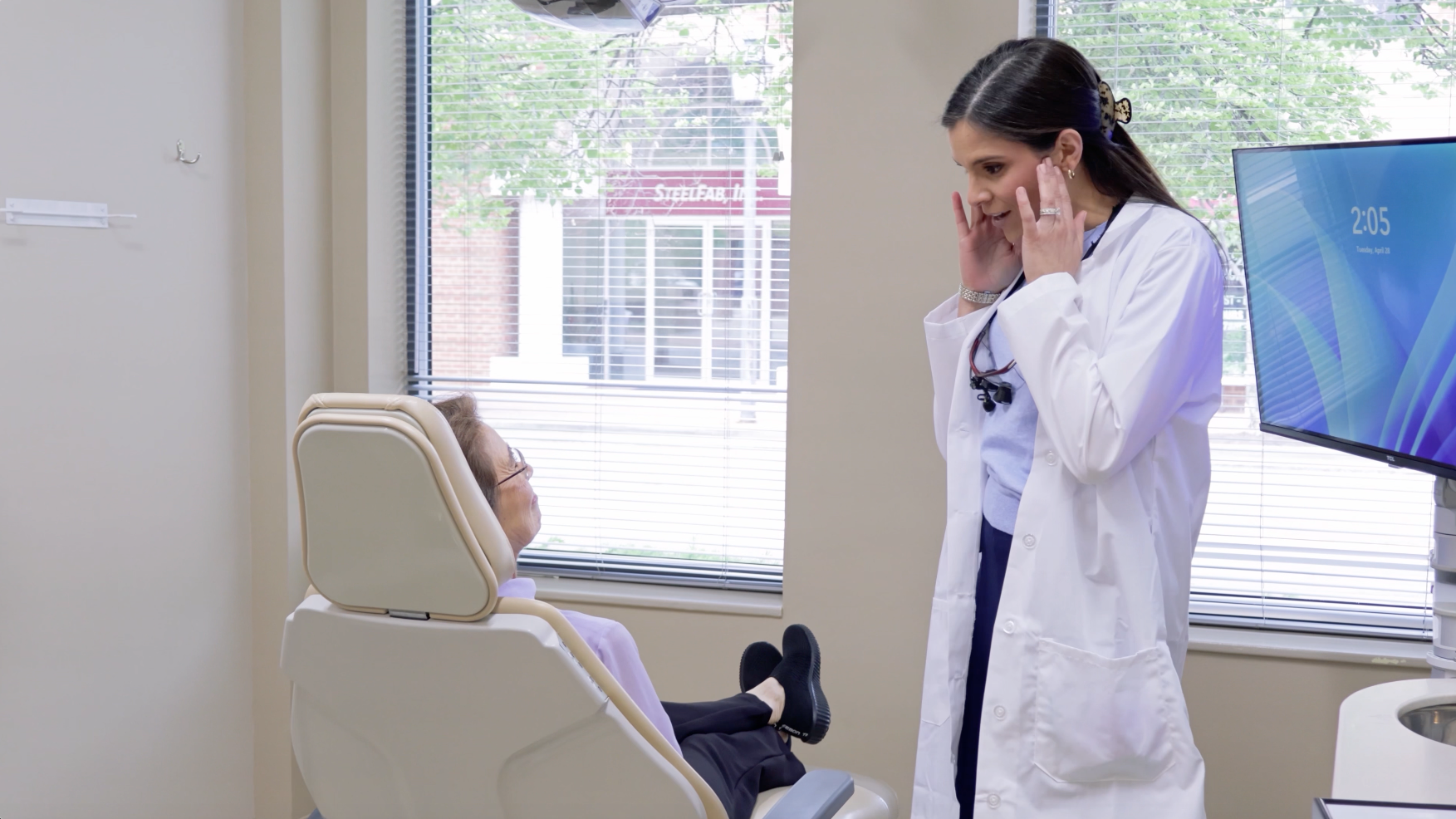 Man in dentist's chair holding jaw, appearing to be in pain, with dental staff in background.