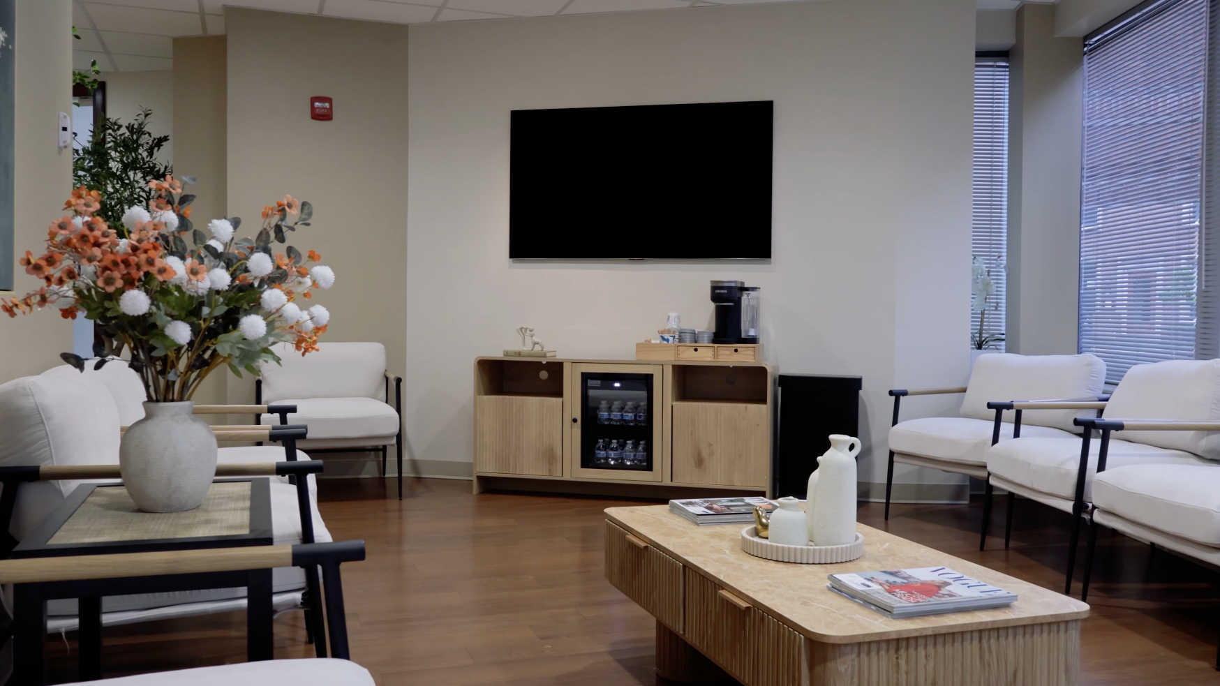 Modern lobby lounge with TV, coffee tables, floral arrangement, and seating.