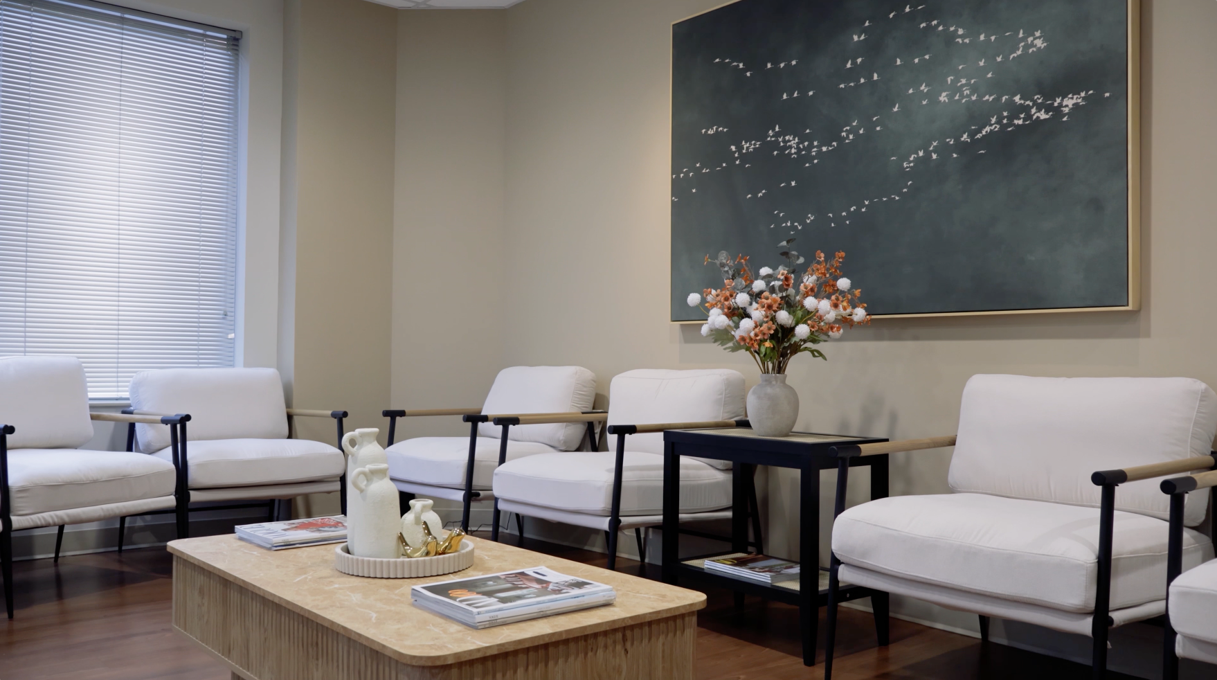 Modern waiting room with white chairs, a coffee table, and a large abstract wall art piece