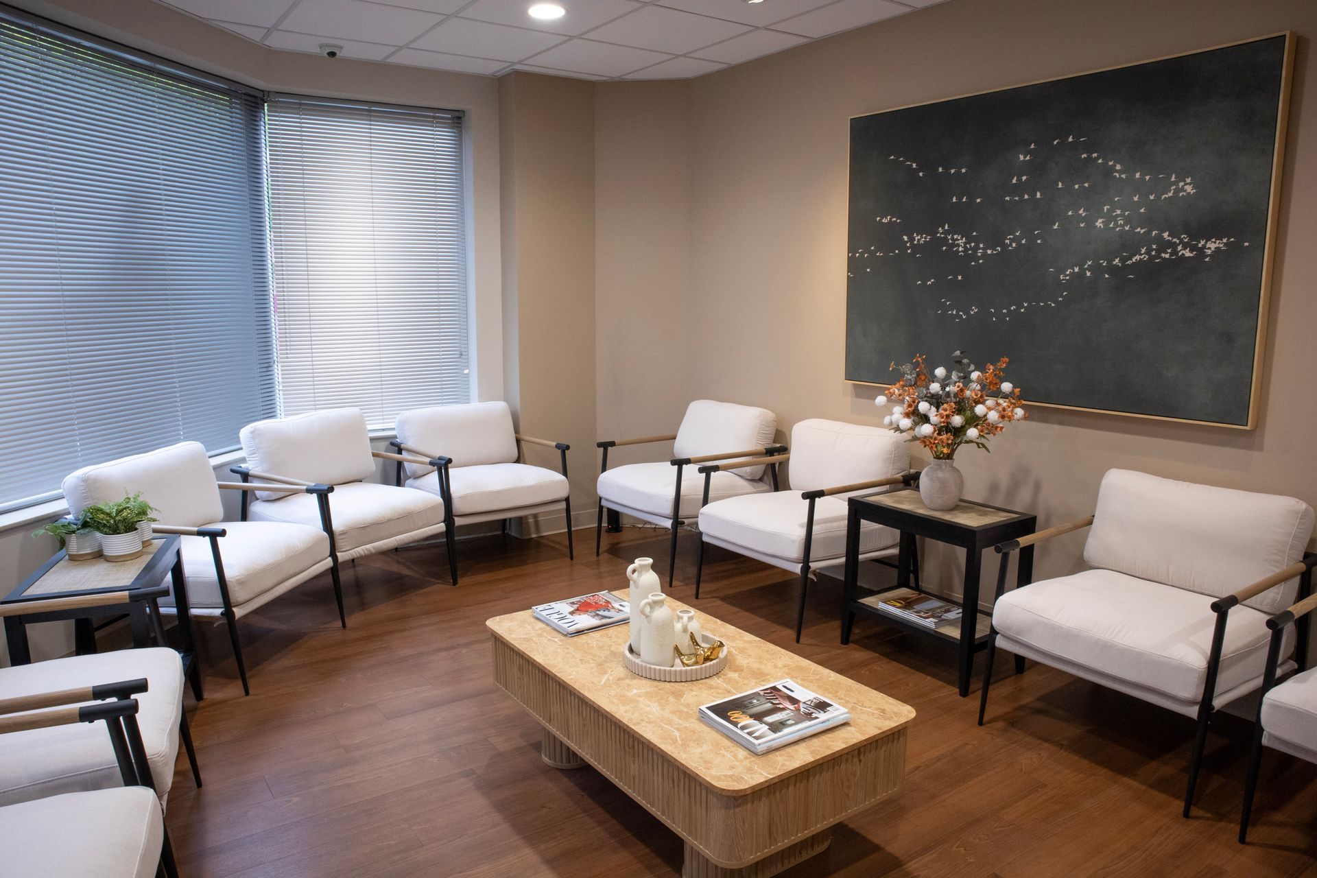 Small meeting room with white chairs, a coffee table, chalkboard, and window blinds.