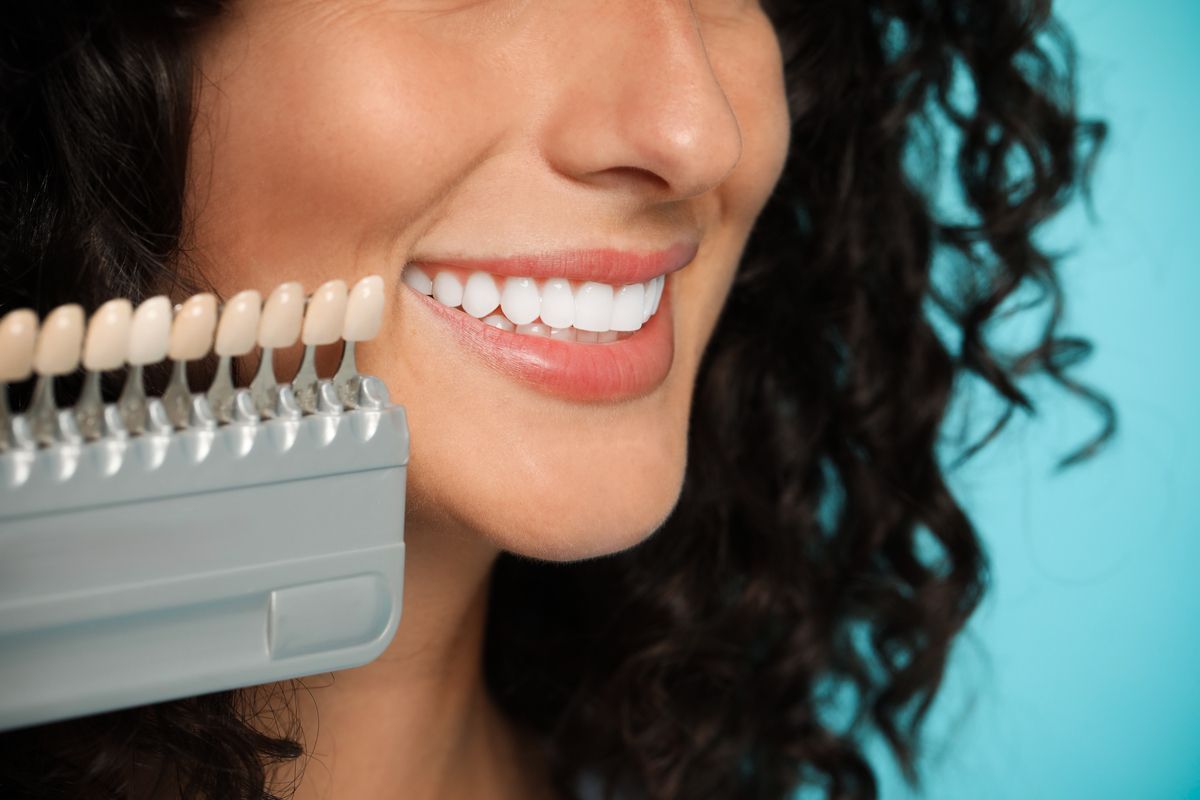 Smiling mouth beside a shade guide for teeth whitening, with turquoise background