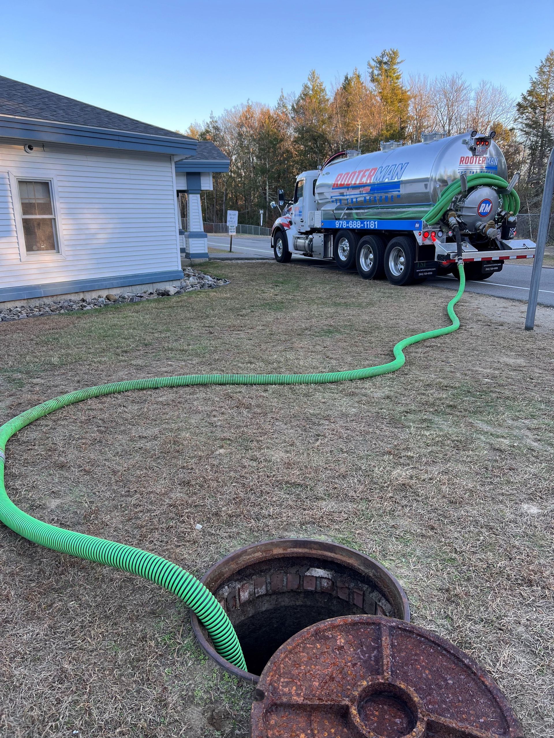 Septic tank truck servicing a residential septic system. Green hose, tank, open manhole.
