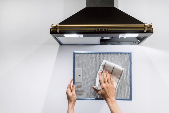 Hands wiping a blue kitchen mat under a stainless steel range hood