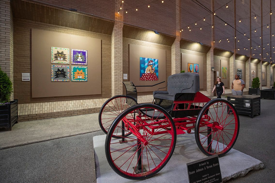 Historic red horse-drawn carriage displayed in a museum hall with framed artwork on the wall