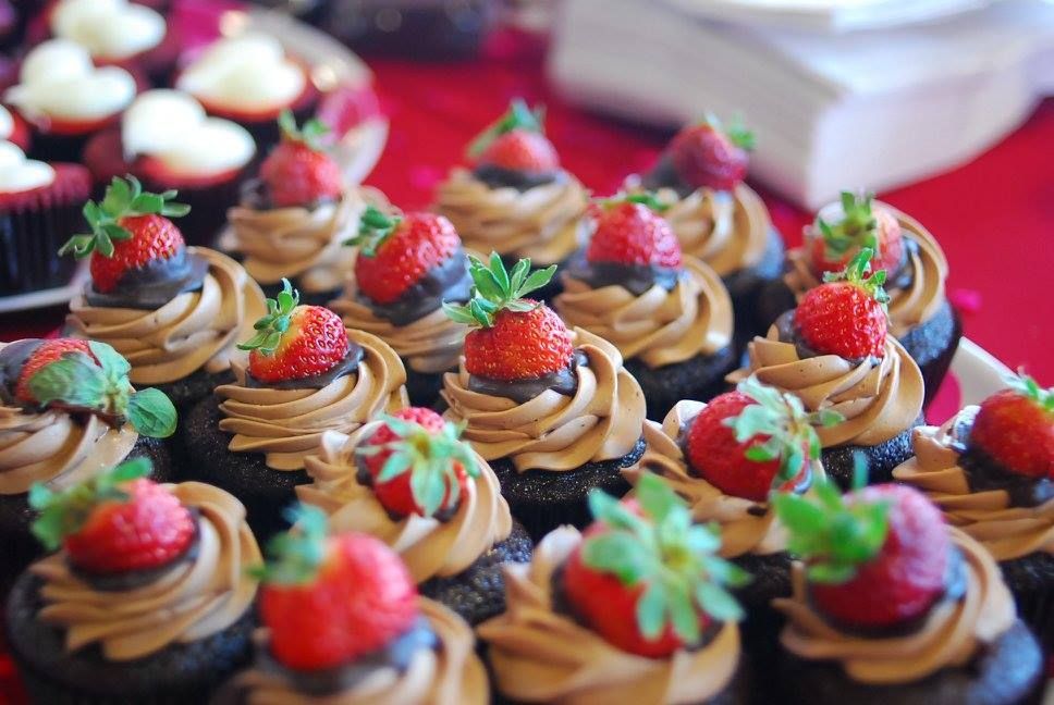 Chocolate cupcakes topped with swirled frosting, strawberries, and blueberries on a pink table
