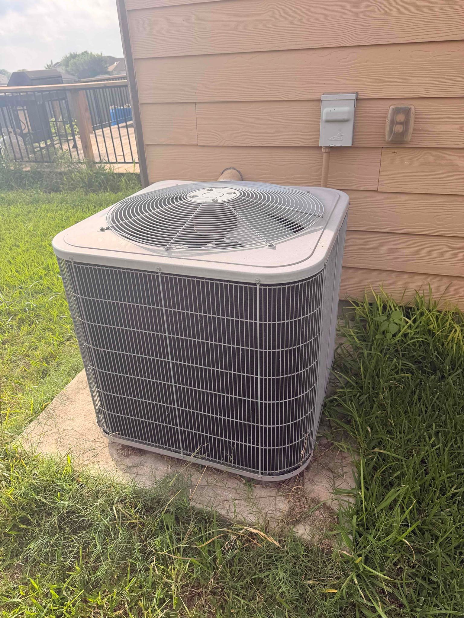 Outdoor air conditioner unit beside a house, on a concrete pad in a grassy yard.