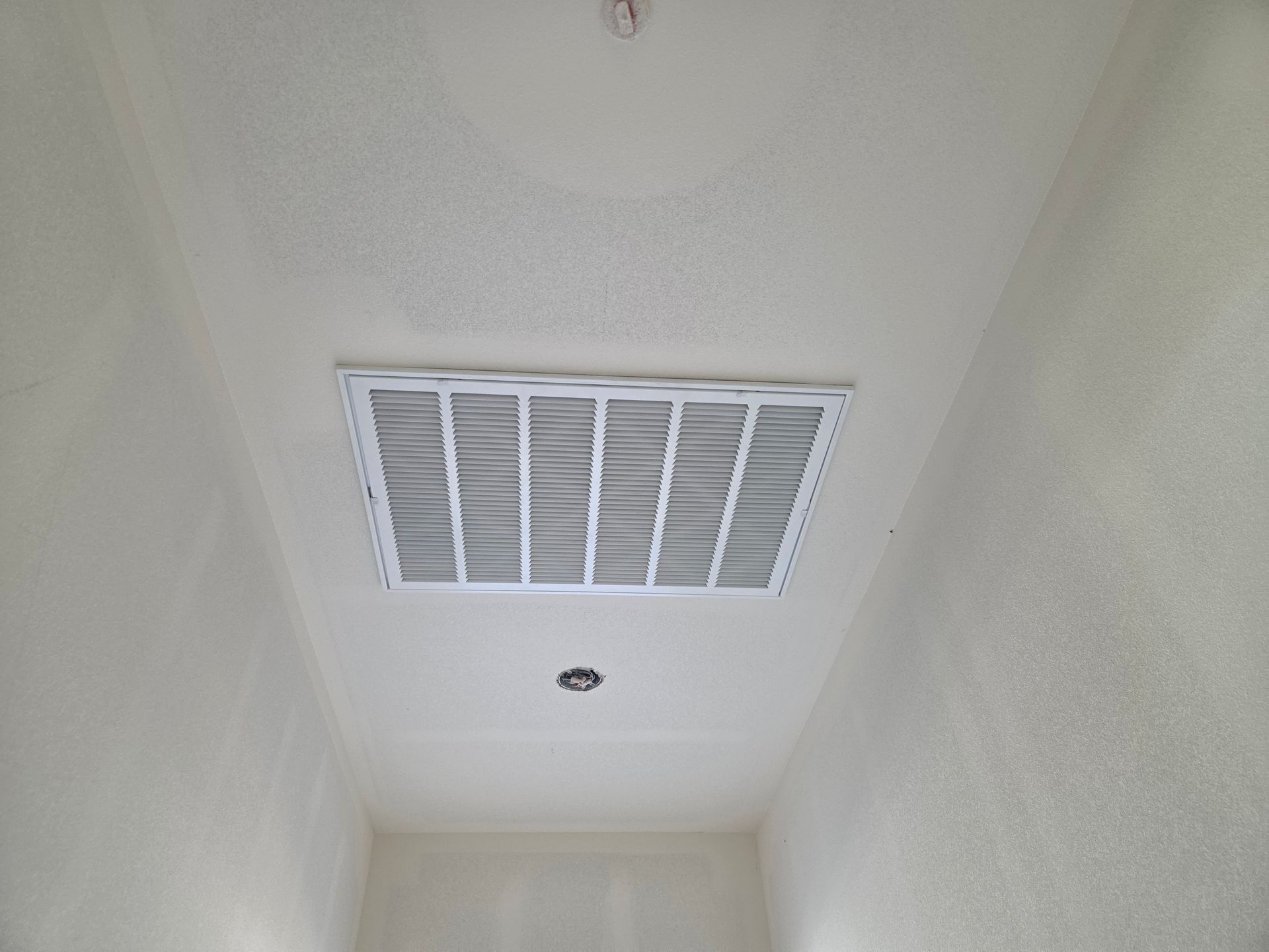 White ceiling vent in a narrow hallway with a light fixture below.