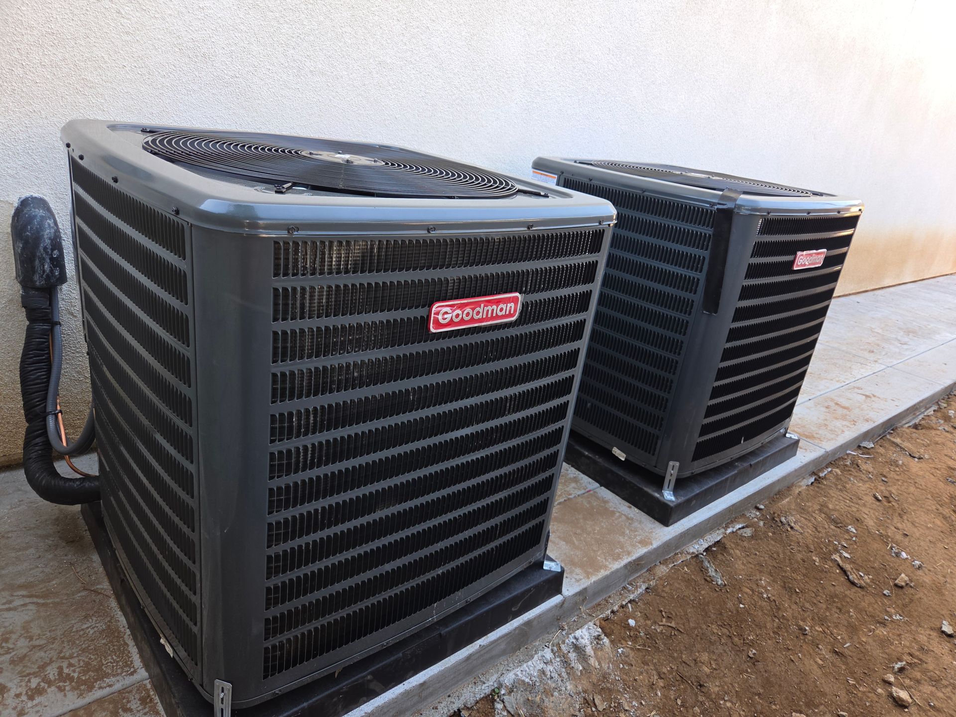 Two black outdoor HVAC units beside a building on a concrete pad