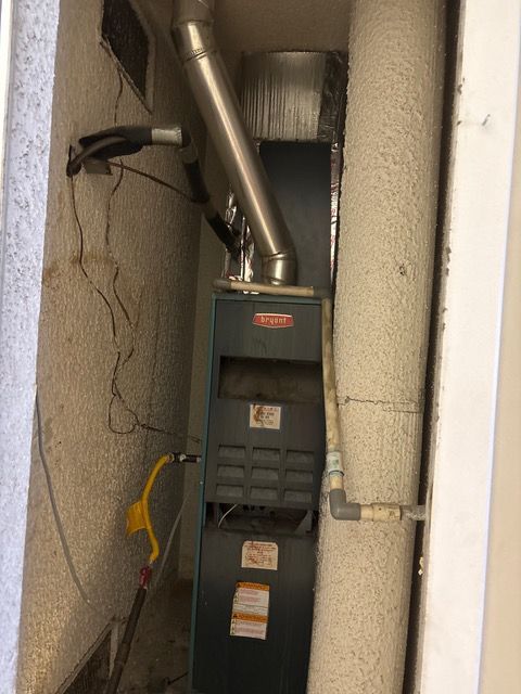 Air handler in a narrow utility closet with exposed pipes and cracked walls