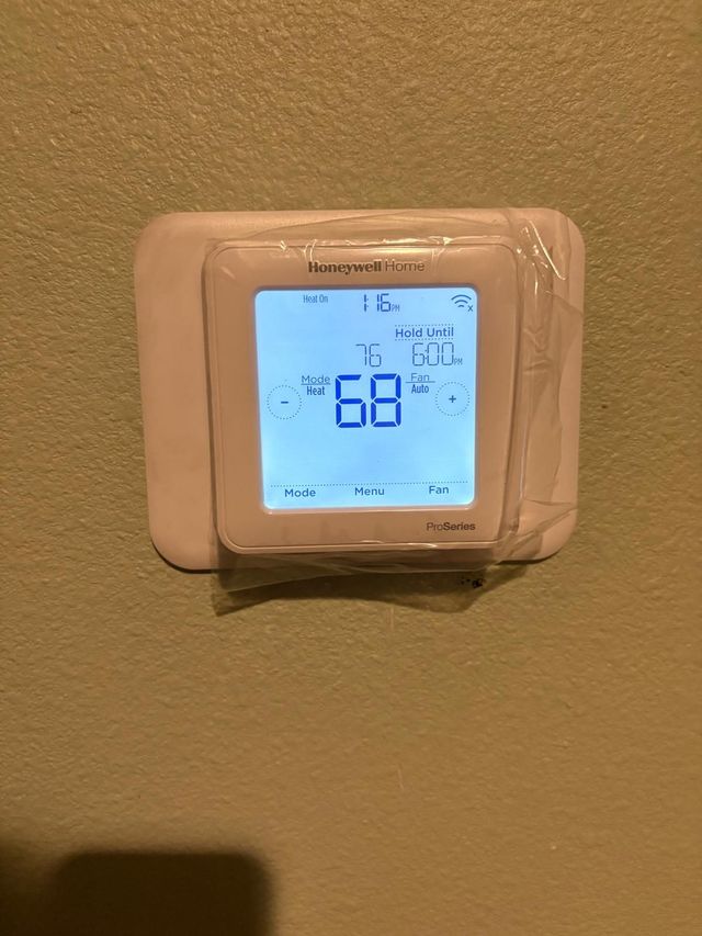 Wall-mounted digital thermostat displaying 68° on a beige wall.