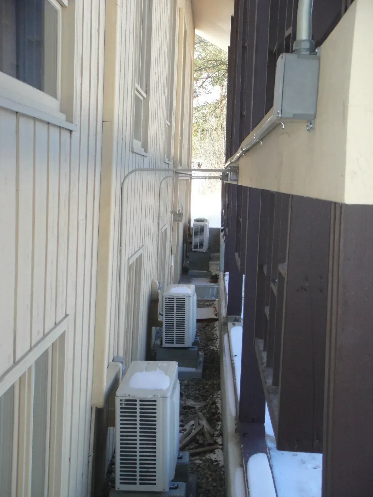 Narrow side yard with several air conditioning units between a light wall and a dark building exterior.