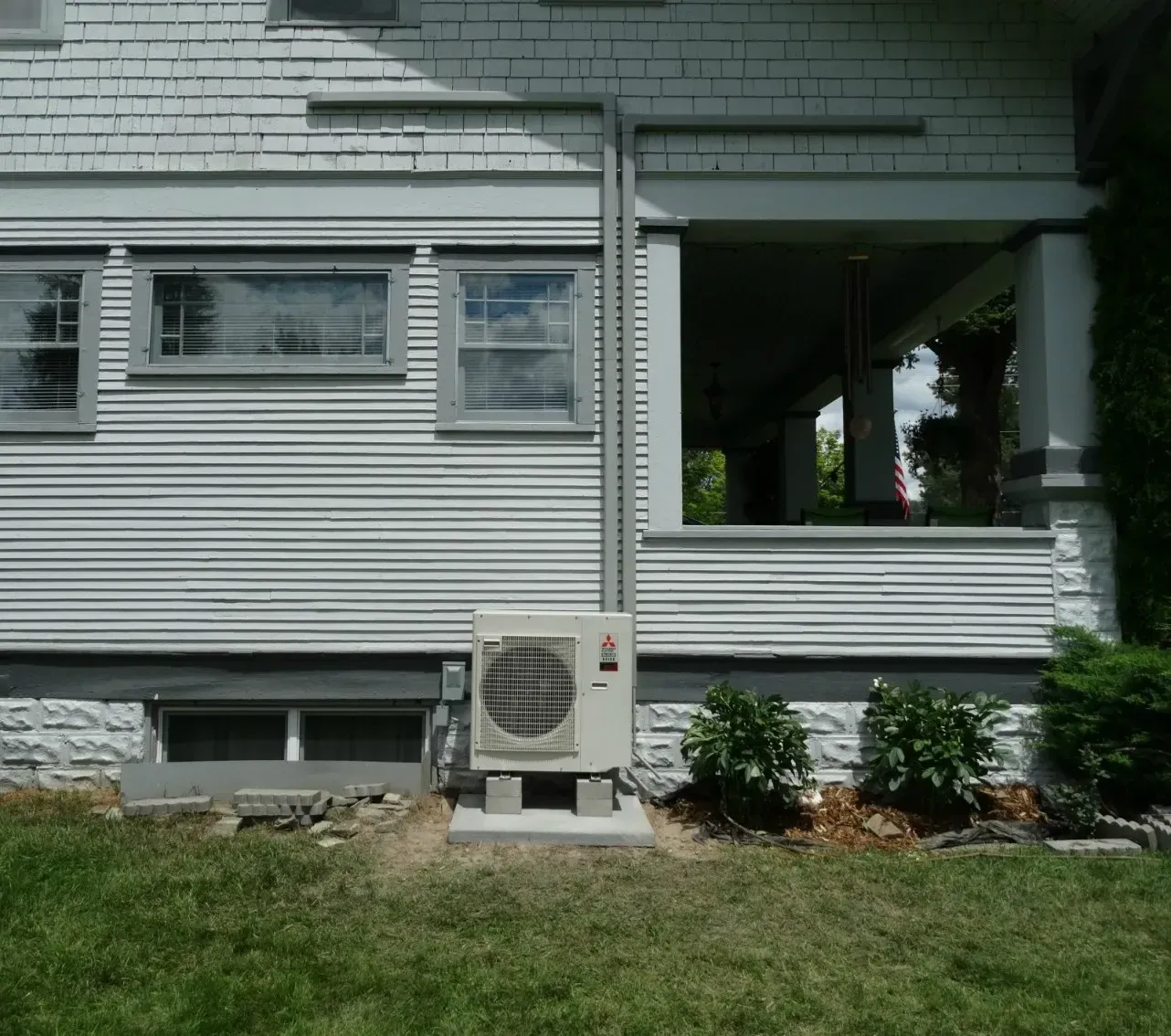 Side view of a gray house with an air conditioner unit, porch, windows, and a grassy yard