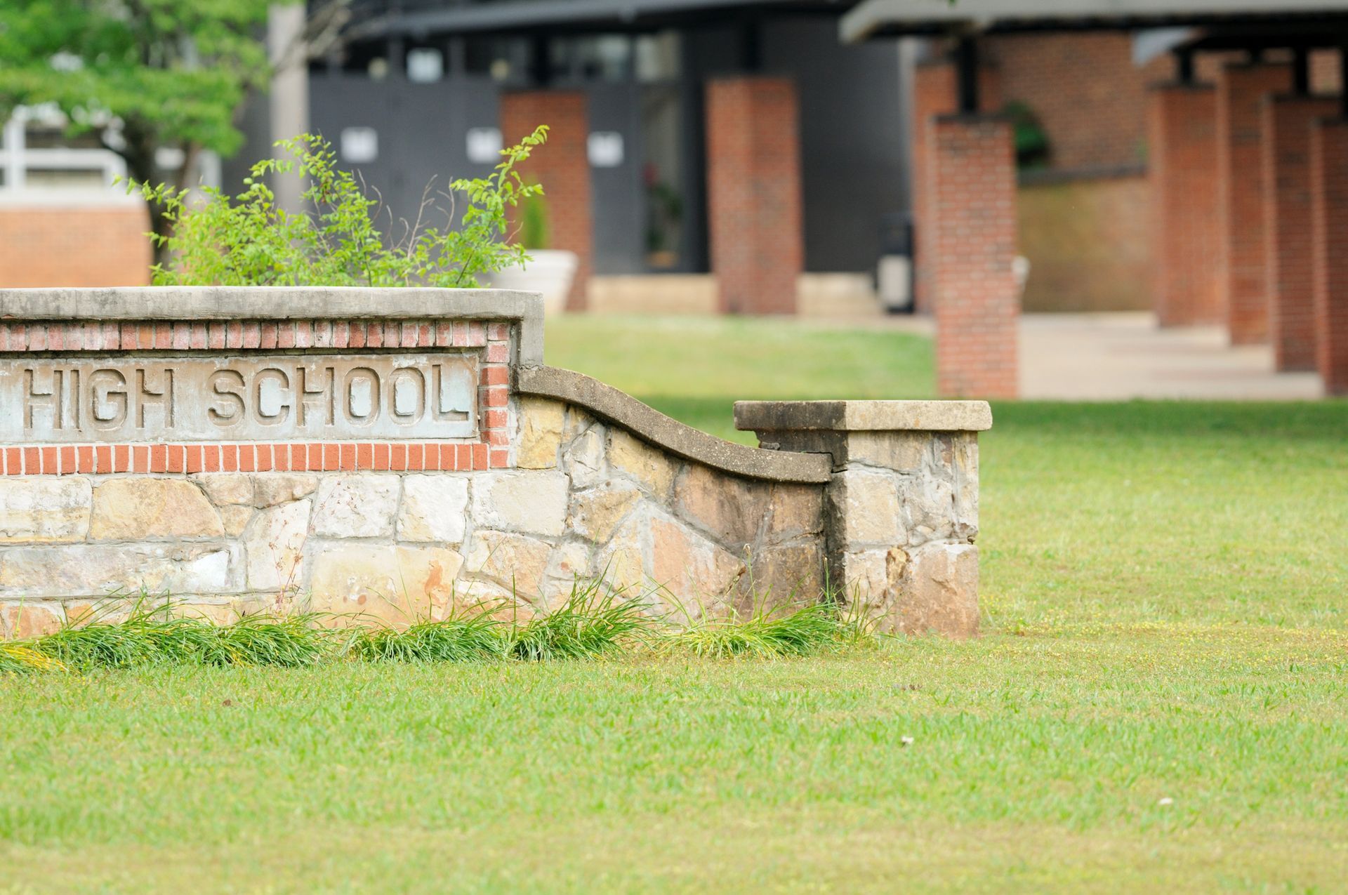 A stone sign with the words High School in front of a grassy area and brick columns