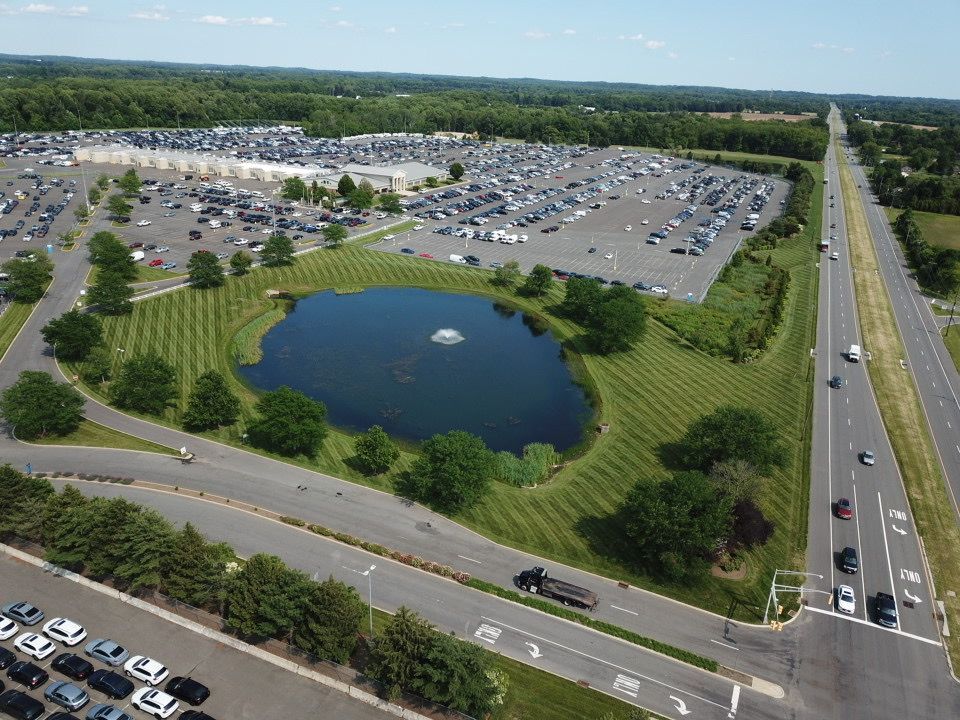 Aerial view of a parking lot, pond with fountain, and highway on a sunny day.
