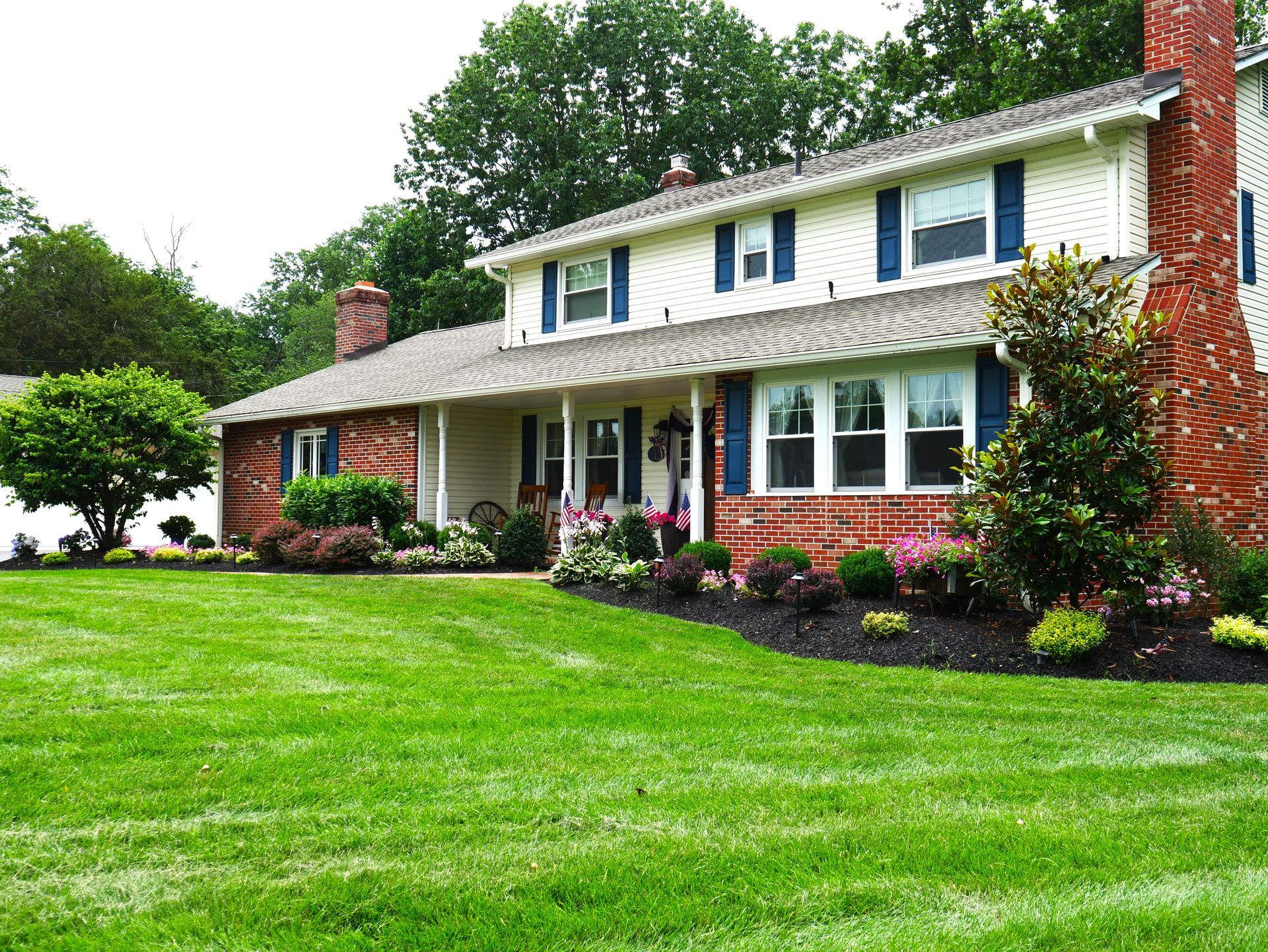 Two-story house with red brick and white siding, blue shutters, and green lawn.
