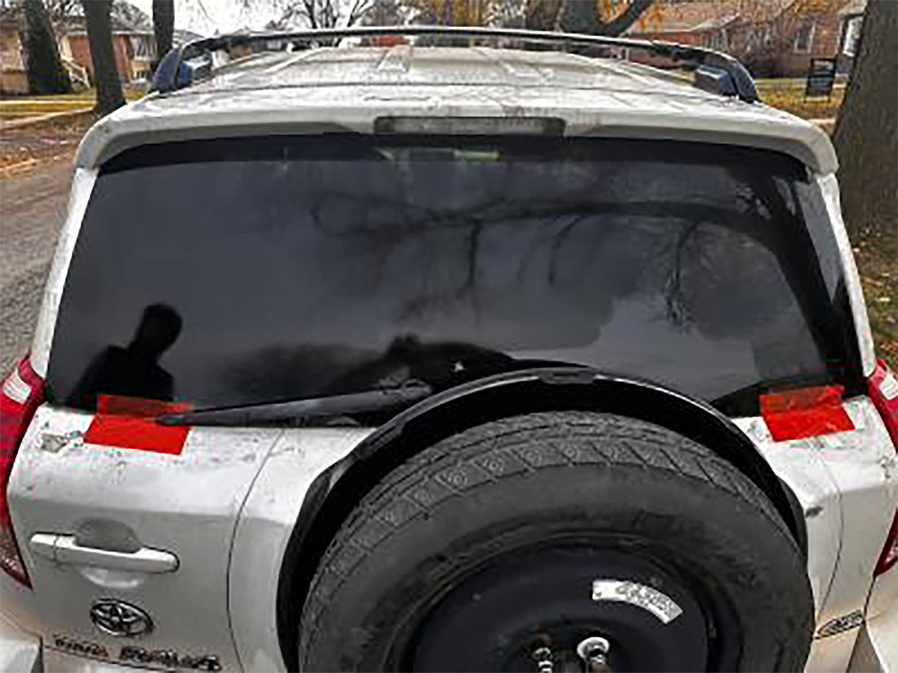 Rear view of a white SUV with tinted windows. Spare tire mounted. Red tape on window edges.