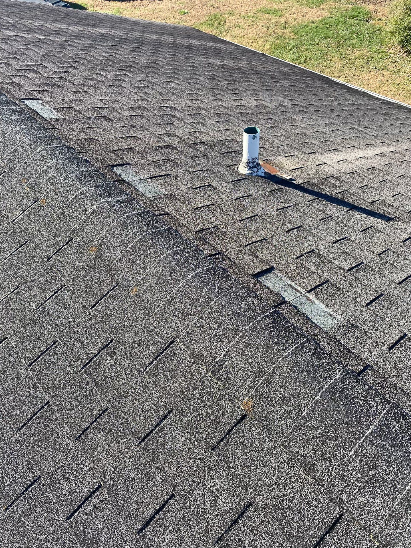 Close-up image of old asphalt shingle roof, viewpoint along the ridge line with missing shingles.