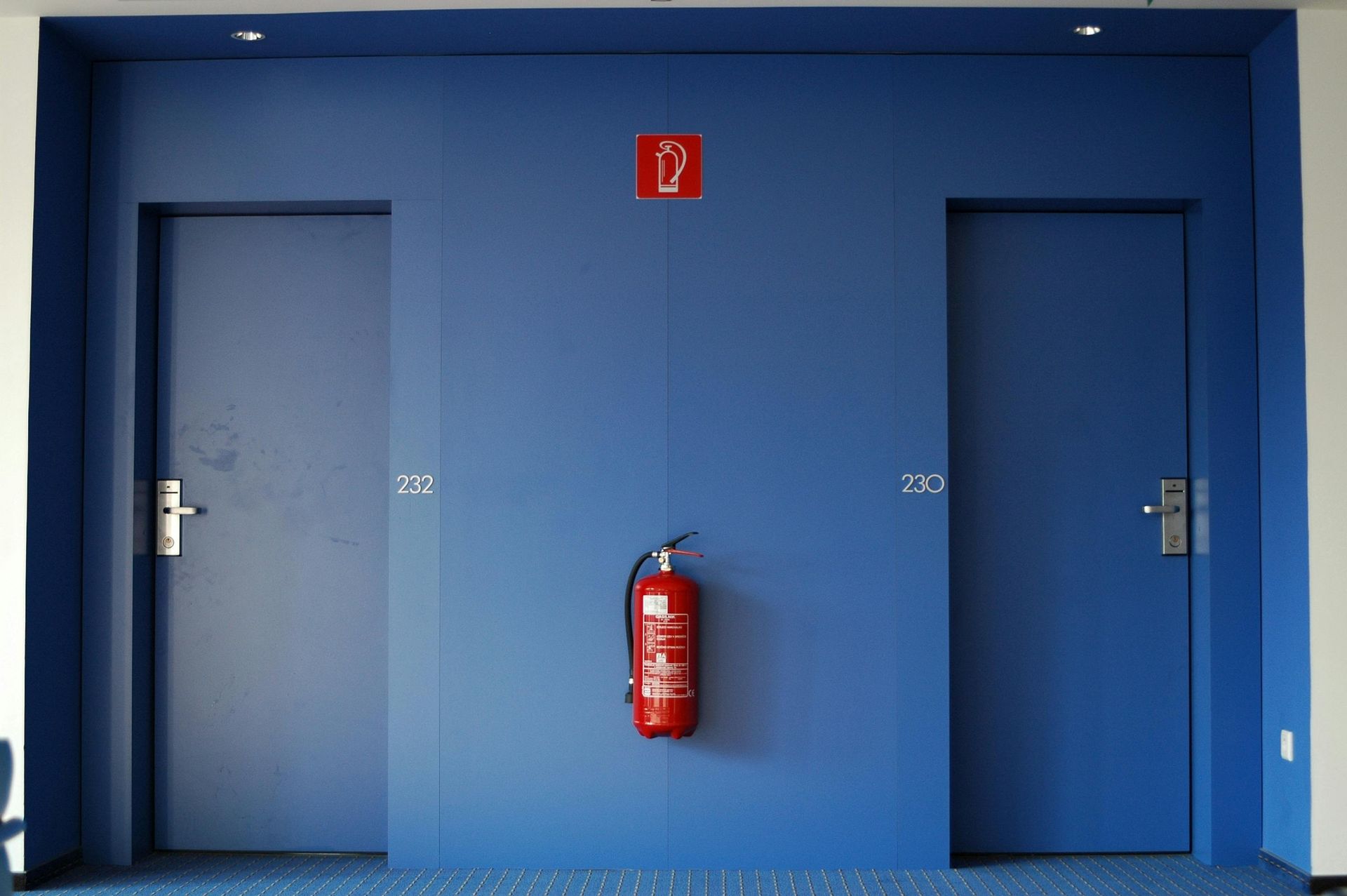 Blue wall with two closed doors, a fire extinguisher, and a fire exit sign.