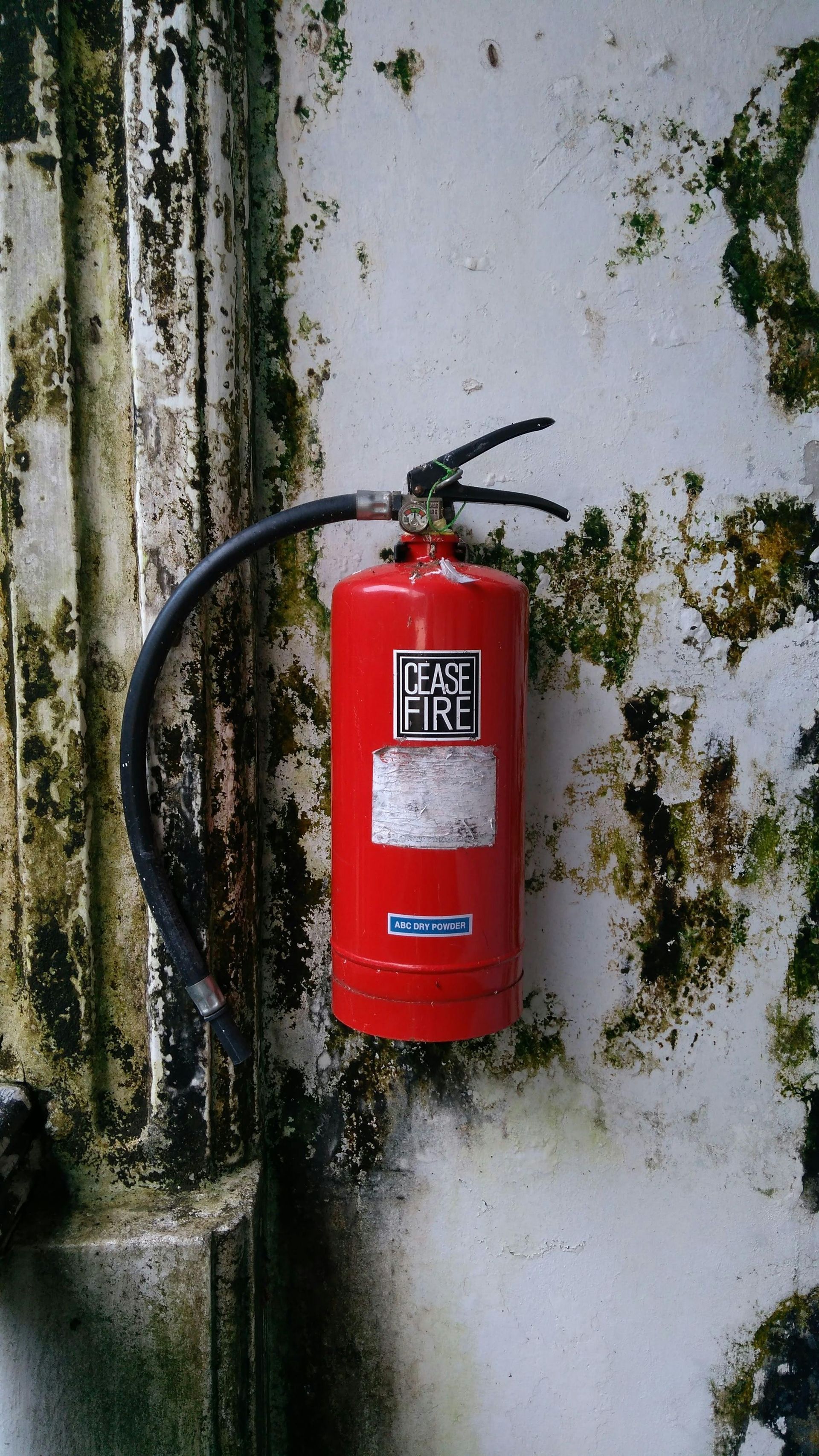 Red fire extinguisher on a dirty white wall with a black hose.