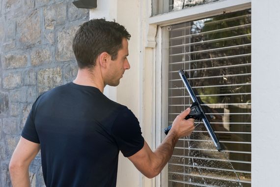 Man cleaning a window with a squeegee beside a stone wall