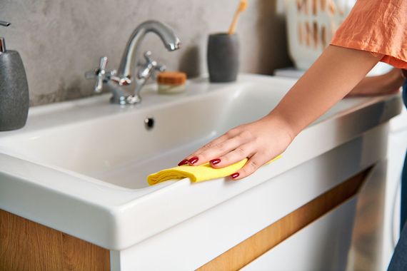 Hand wiping a white bathroom sink with a yellow cloth under a faucet