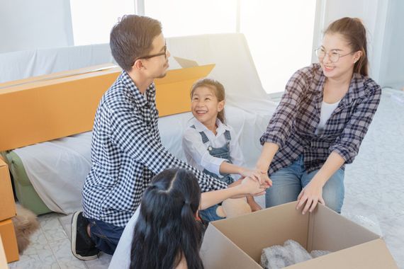 Family unpacking boxes in a bright bedroom, smiling and stacking hands together.