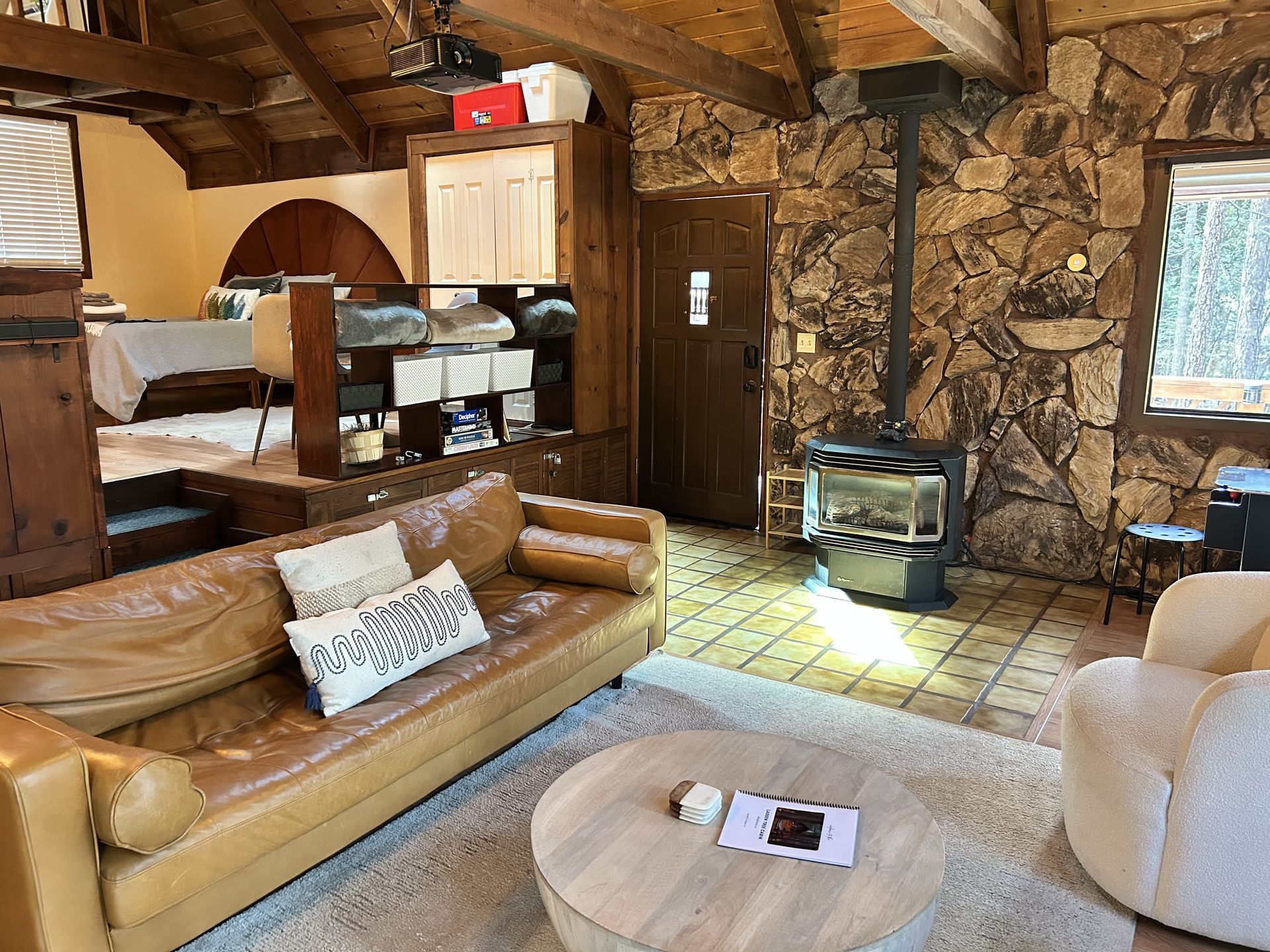 Cozy rustic living room with leather sofa, round coffee table, cream chair, and stone fireplace.