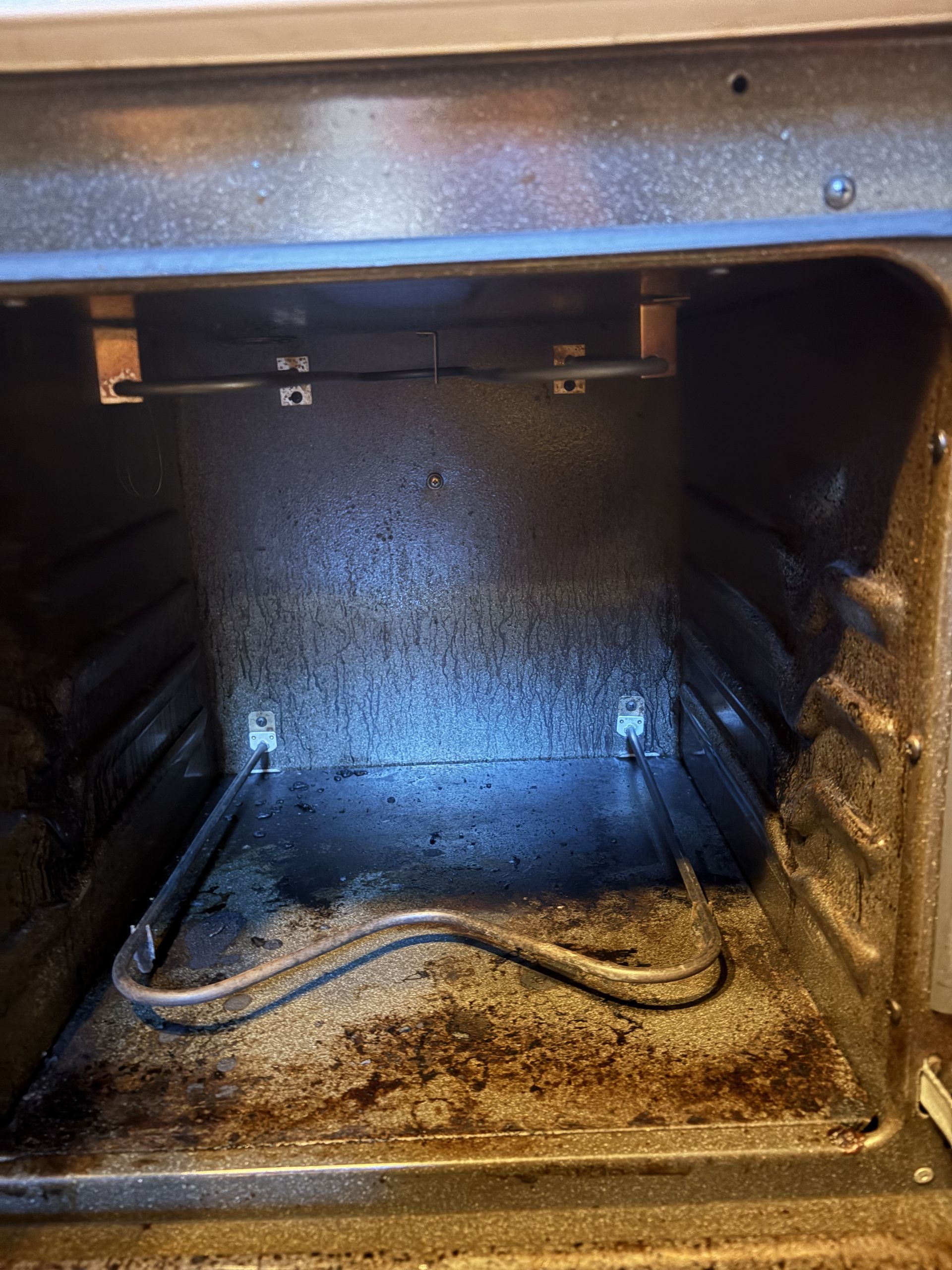 Empty black appliance interior with a dirty bottom and a power cord lying across it