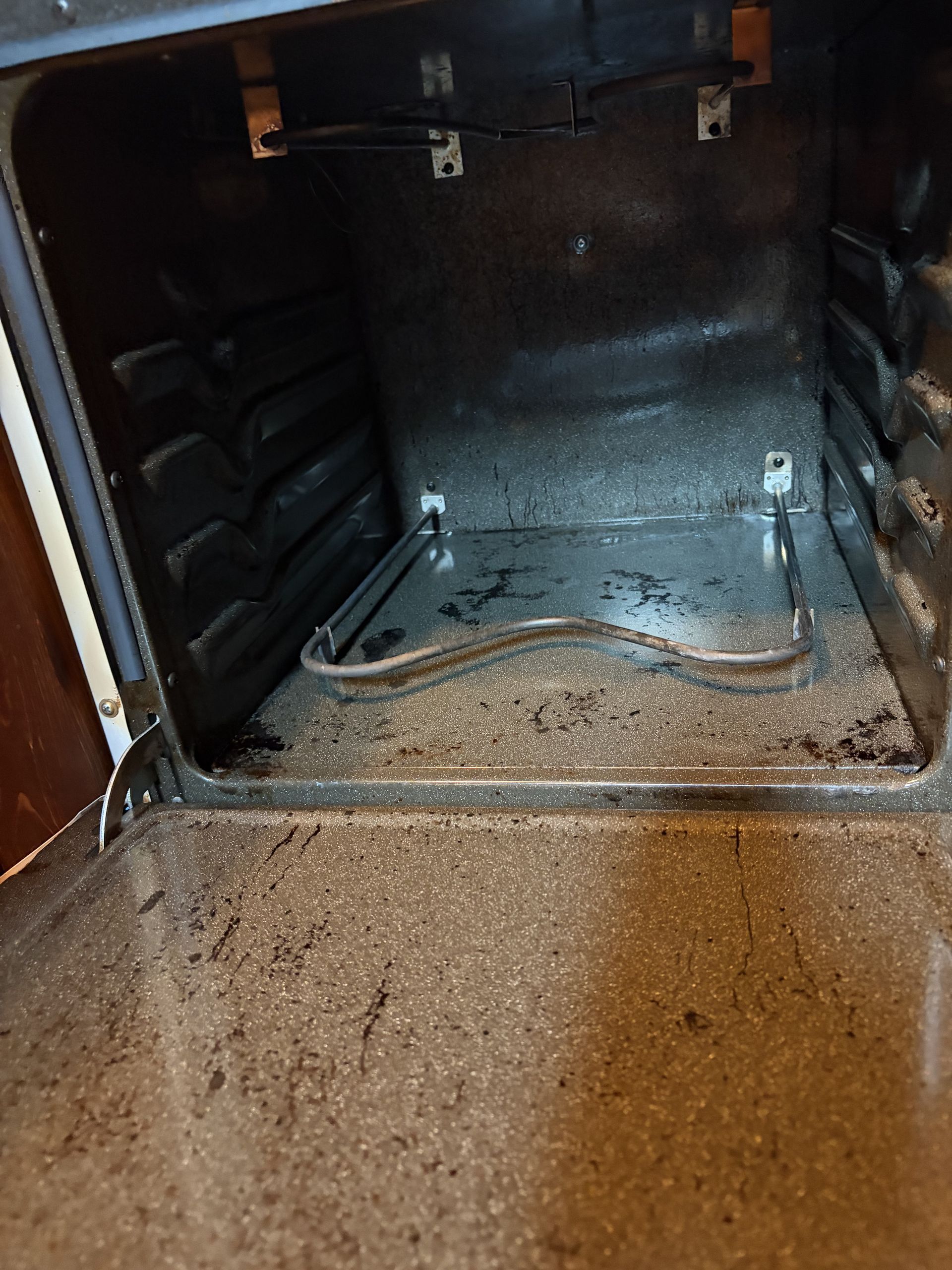 Dirty oven interior with crumbs and burnt residue on the bottom and sides