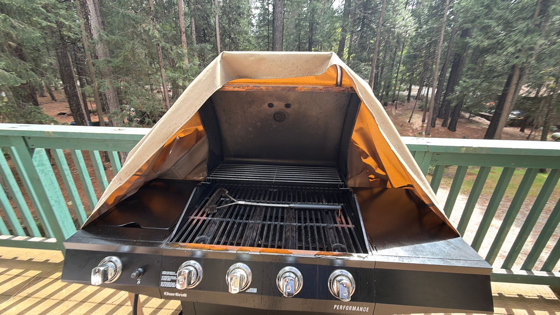 Stainless steel gas grill with lid open and control knobs visible on a deck
