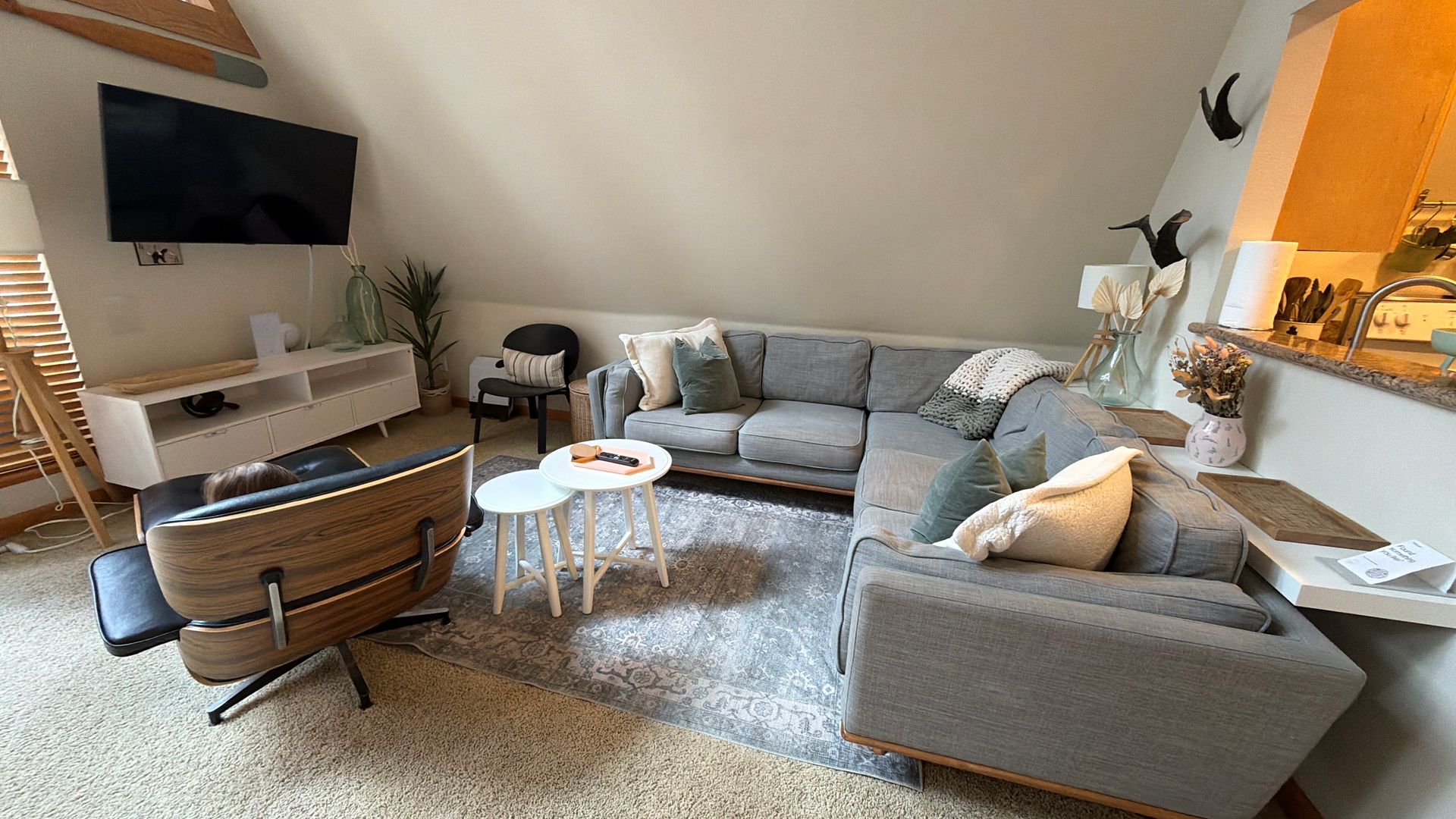 Bright living room with gray sectional sofa, armchair, round coffee tables, wall TV, and plush rug