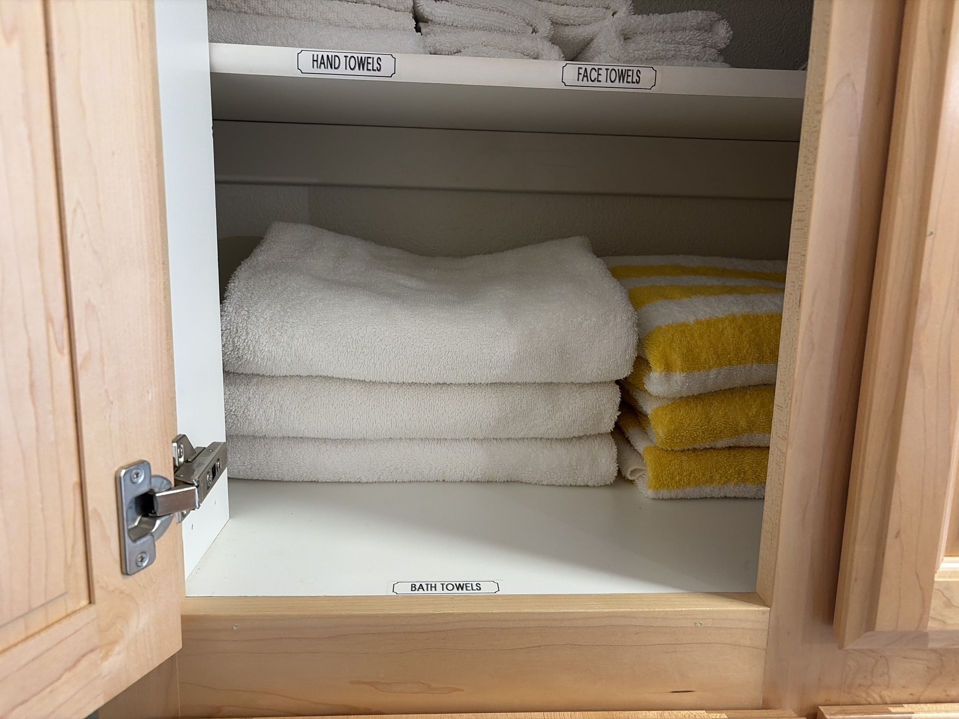 Open wooden cabinet with neatly folded white and yellow towels on shelves
