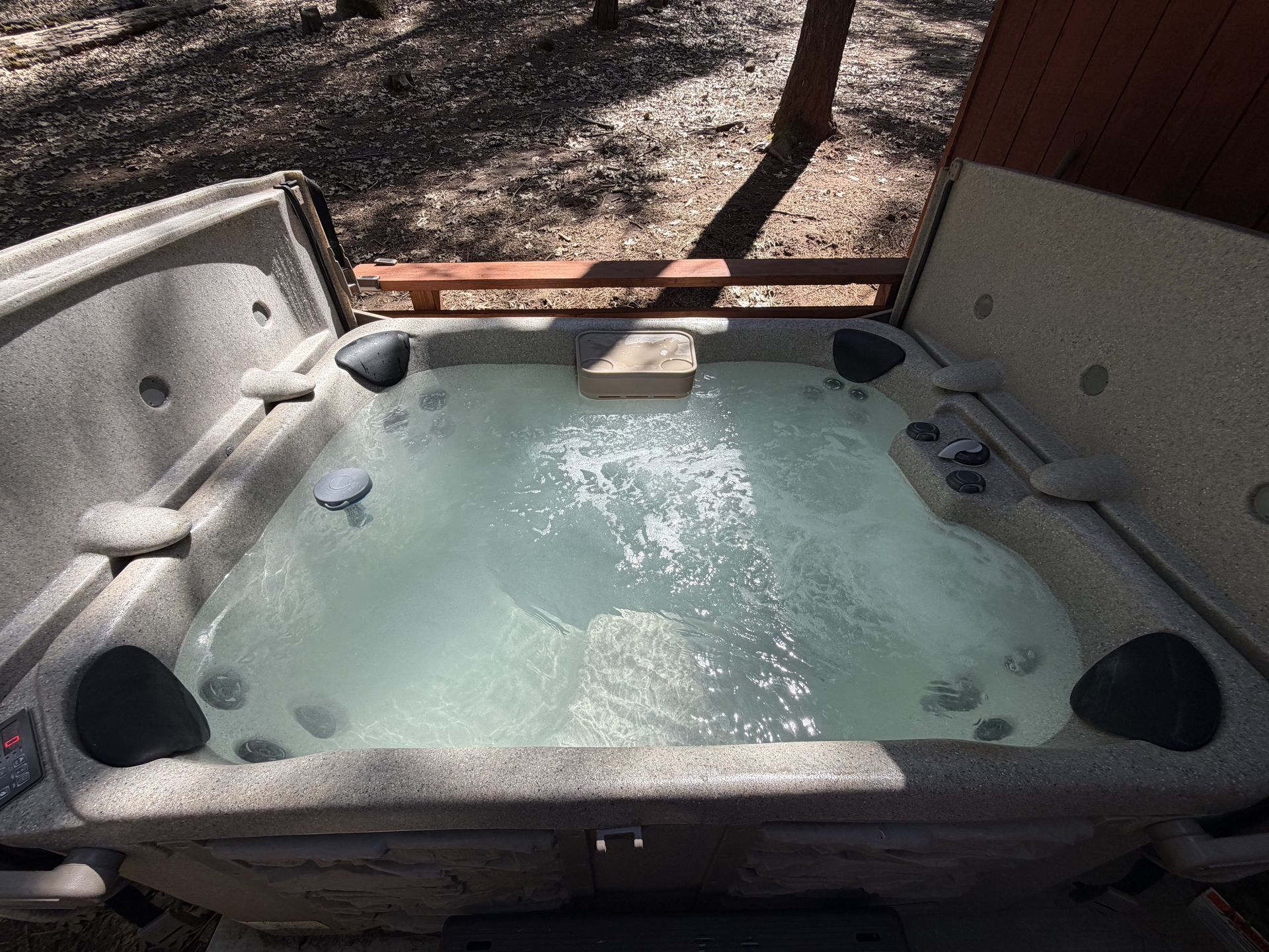 Outdoor hot tub with cloudy water, surrounded by a wooden deck and covered seating area