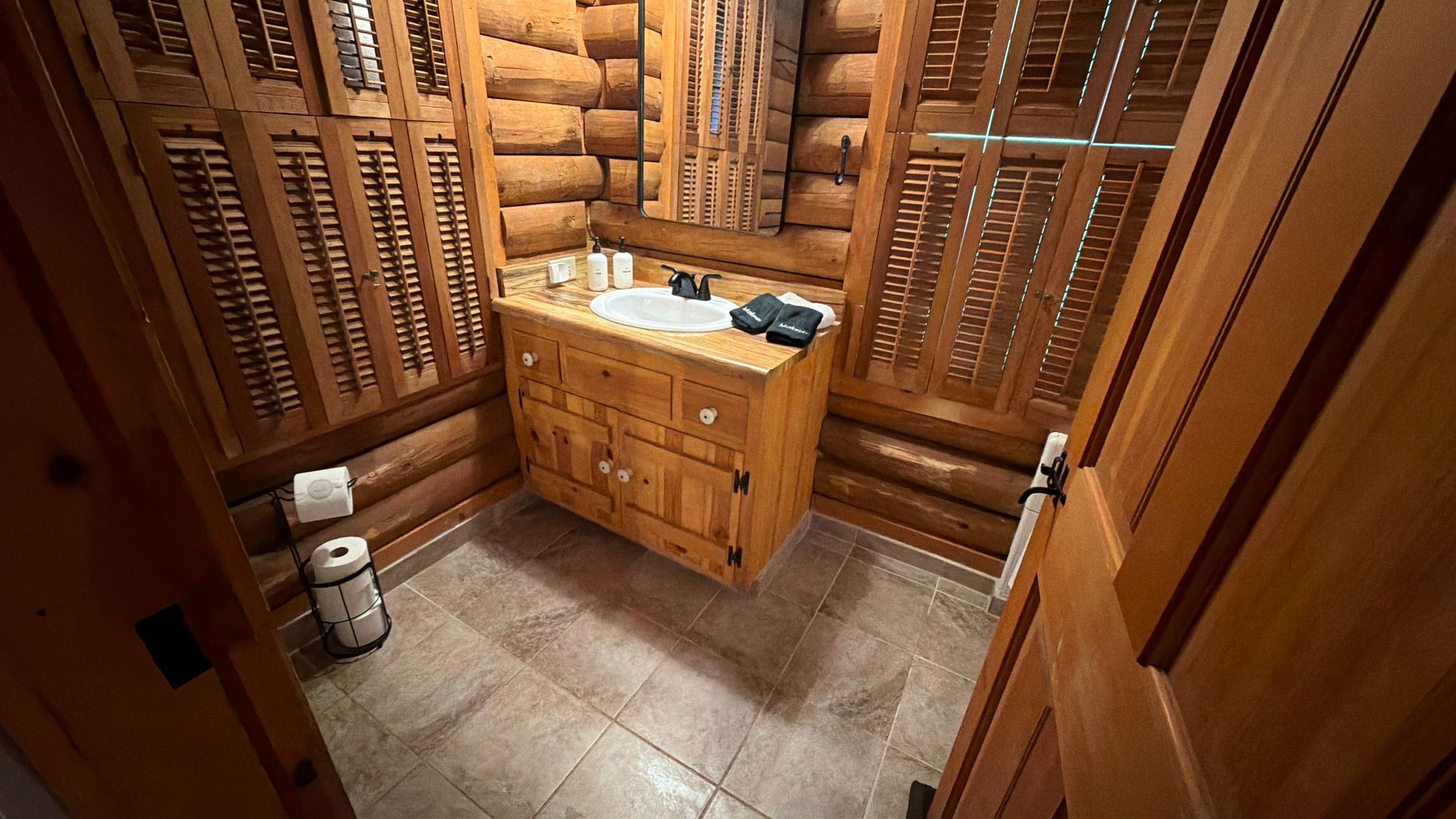 Wooden sauna room with a stone floor, bench, and a central wooden cabinet with towels and items on top.