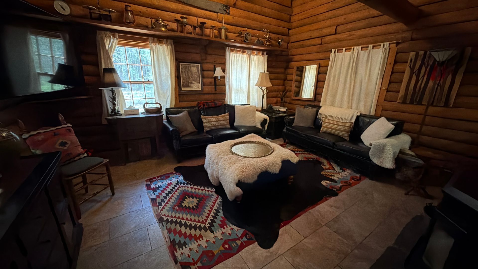 Cozy log cabin living room with dark leather furniture, patterned rug, and daylight through windows.