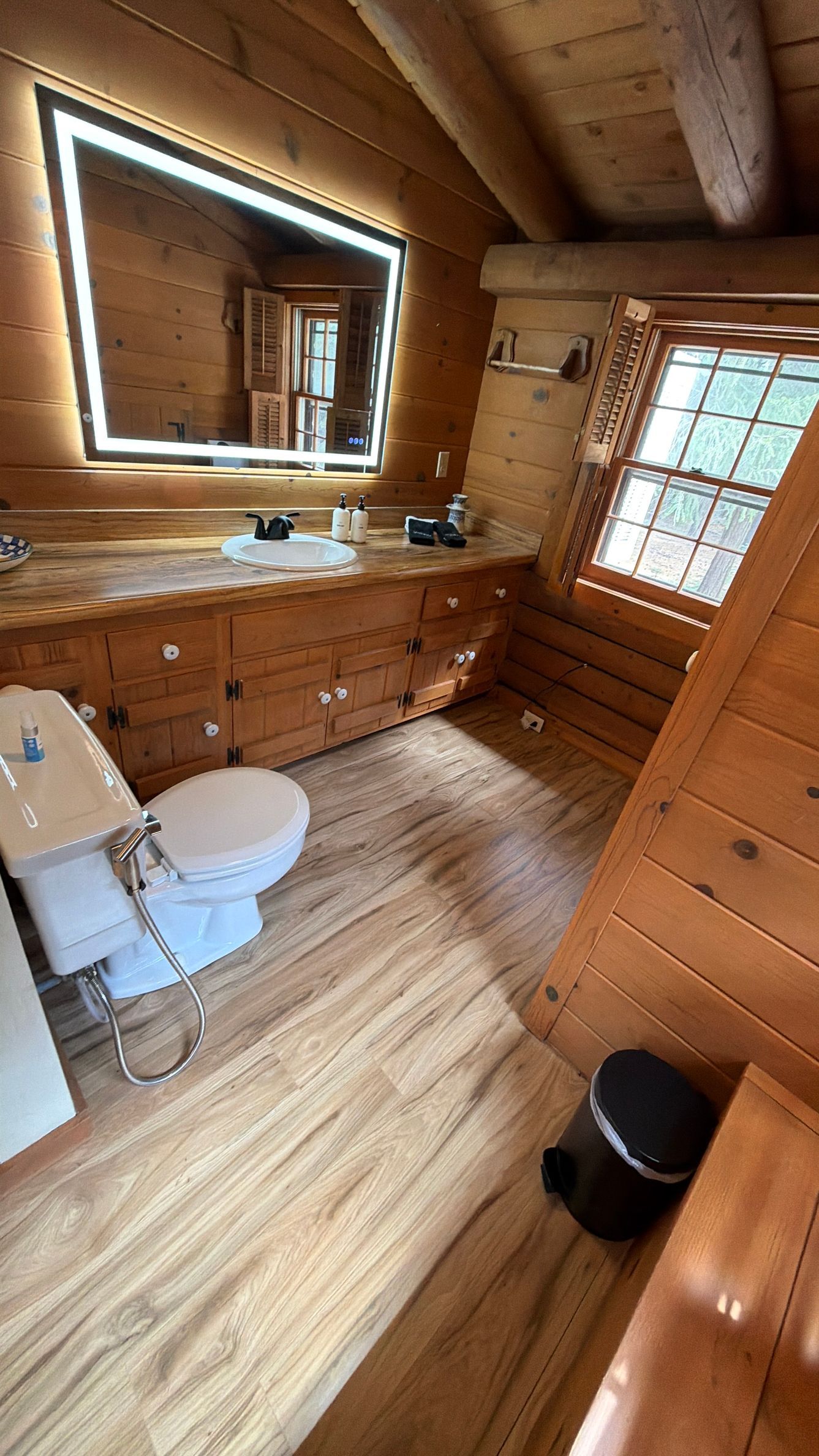 Wood-paneled bathroom with sink, mirror lights, toilet, bathtub, and skylight window.