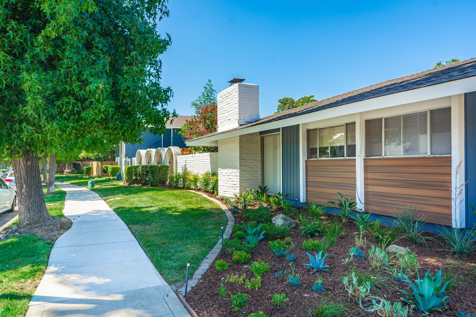 Sunny suburban house exterior with curved sidewalk, green lawn, and landscaped front garden
