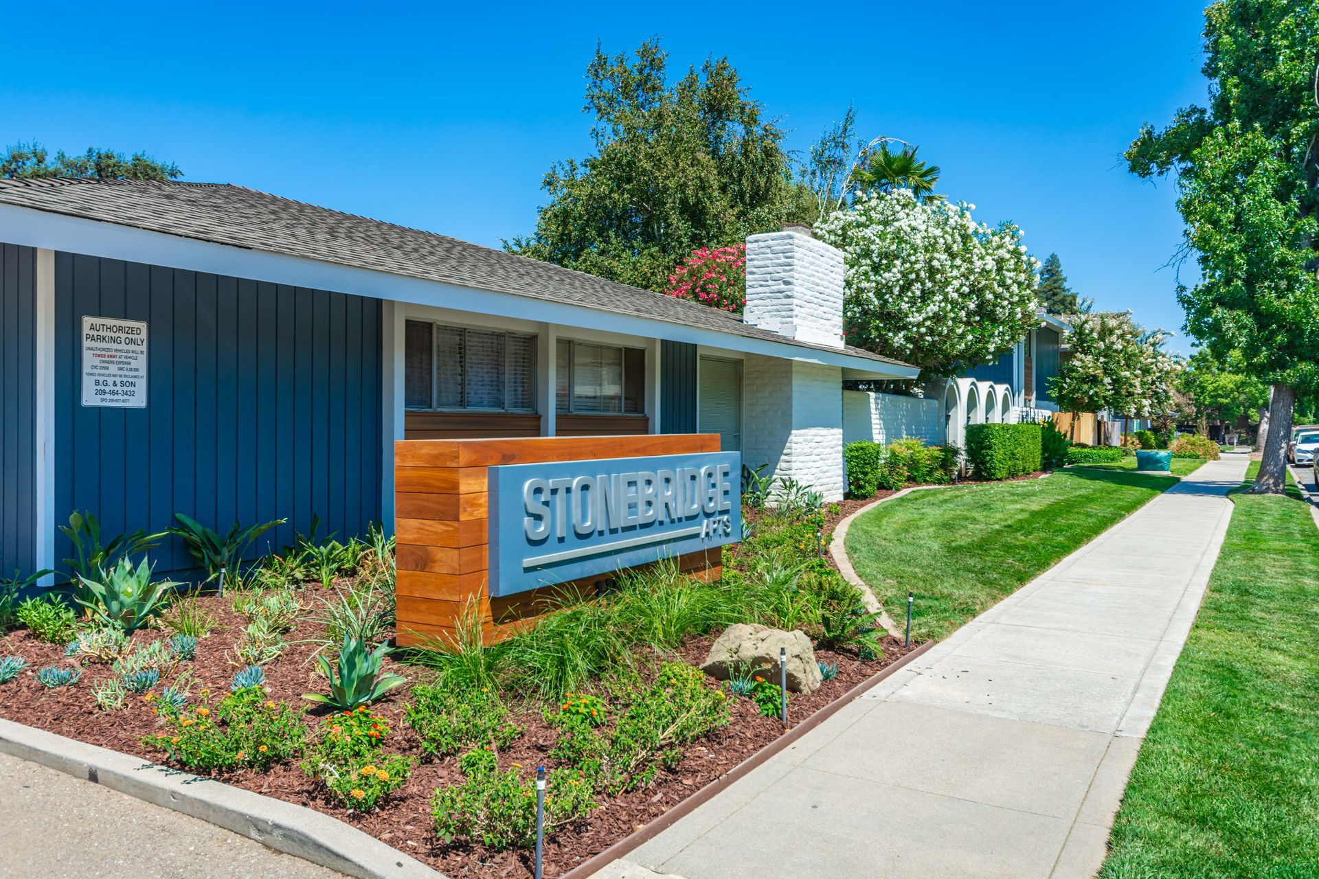 Stonebridge apartment building sign beside a blue exterior, landscaped walkway, and trees on a sunny day