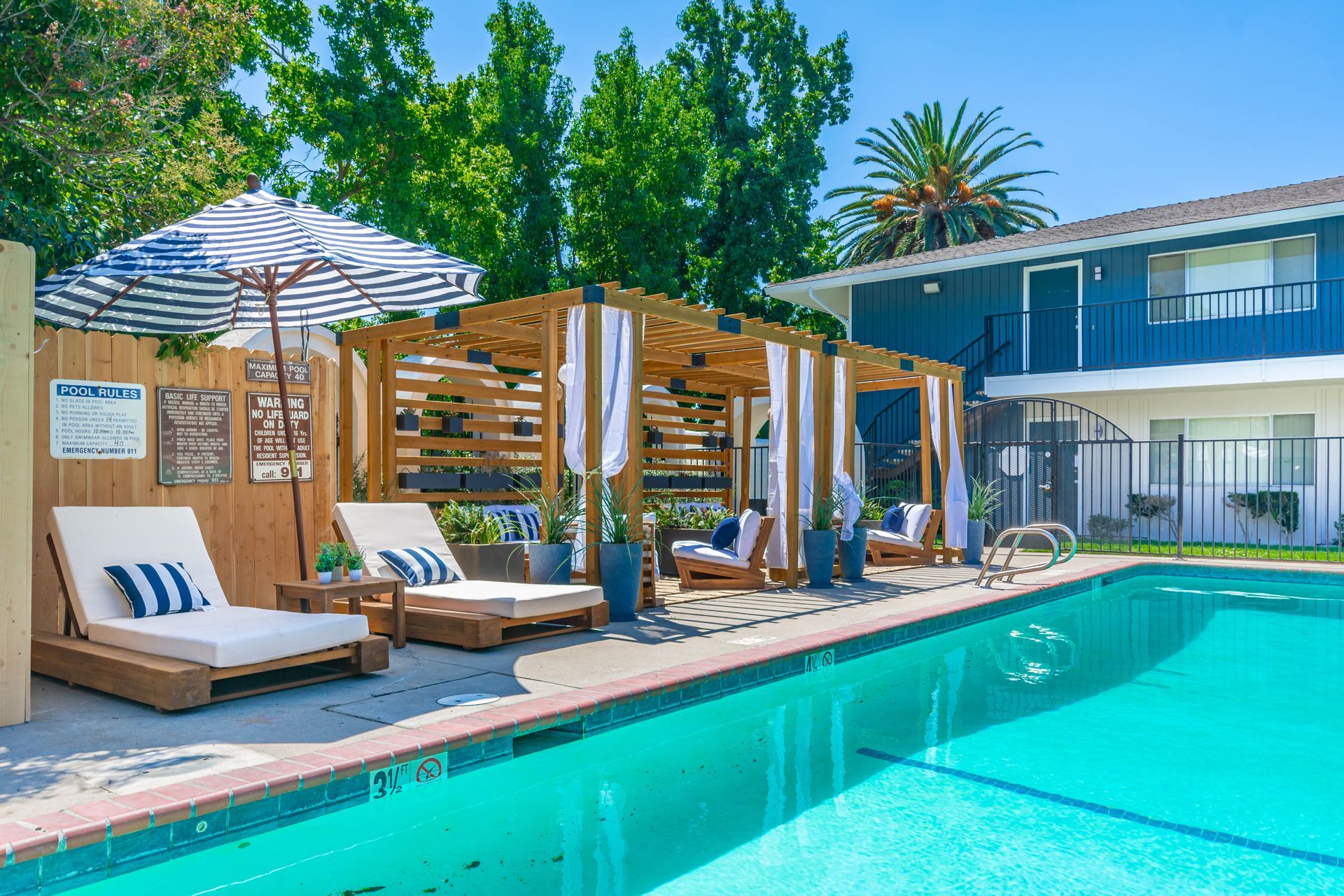 Sunny poolside patio with striped loungers, wooden cabanas, and turquoise water at a hotel or resort