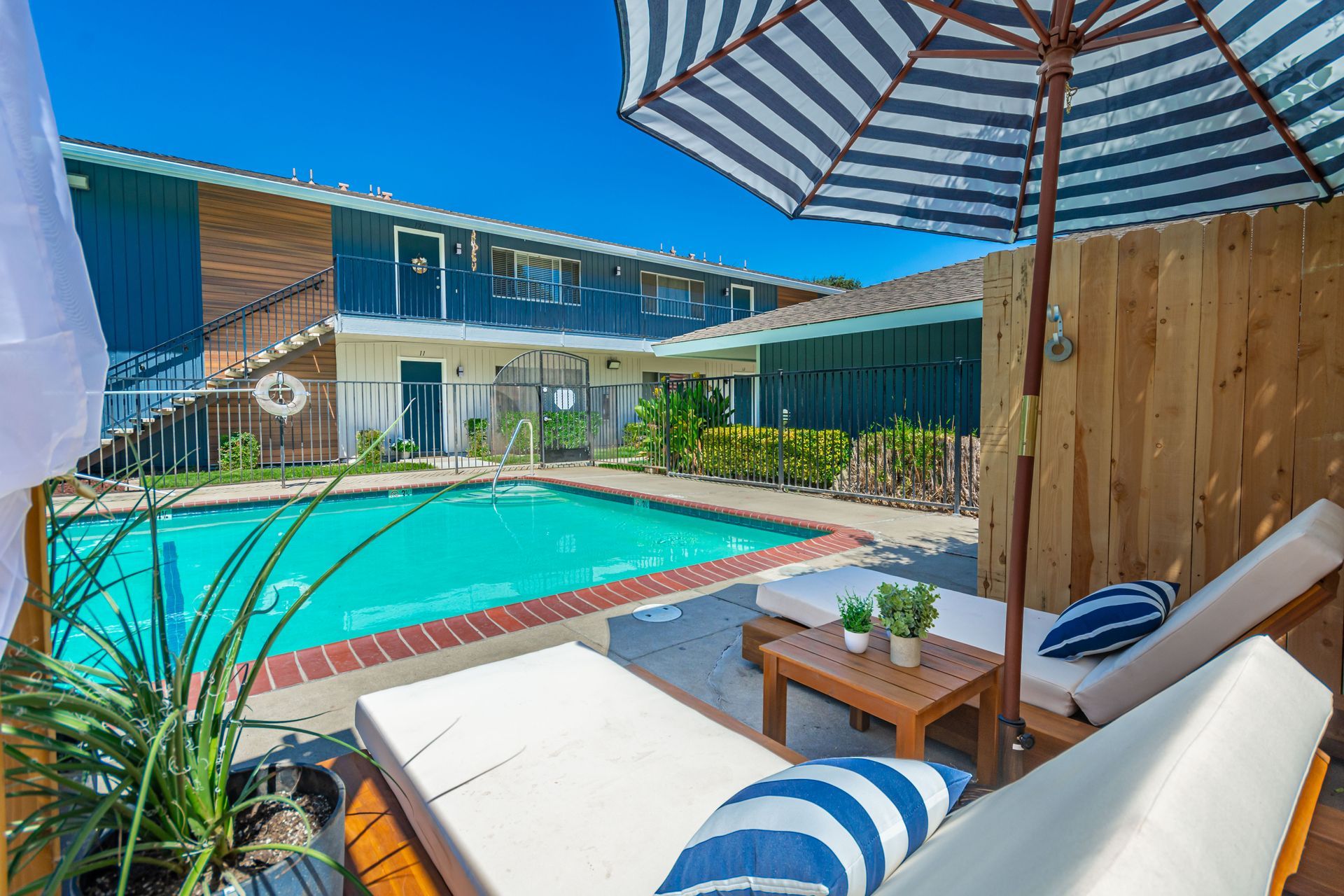 Sunny backyard pool with blue water, striped umbrellas, and a modern house patio.