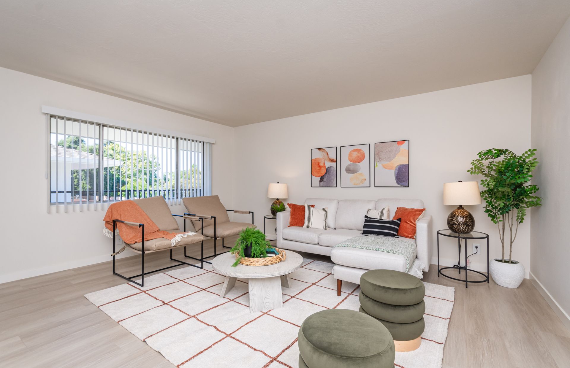 Bright modern living room with white sofa, orange chairs, rug, coffee table, and potted plant