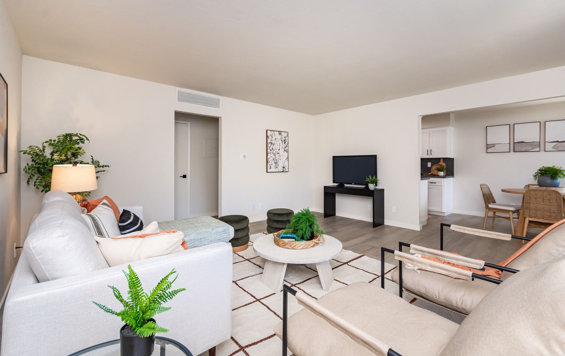 Bright living room with beige sofas, a TV on a small stand, potted plants, and neutral decor