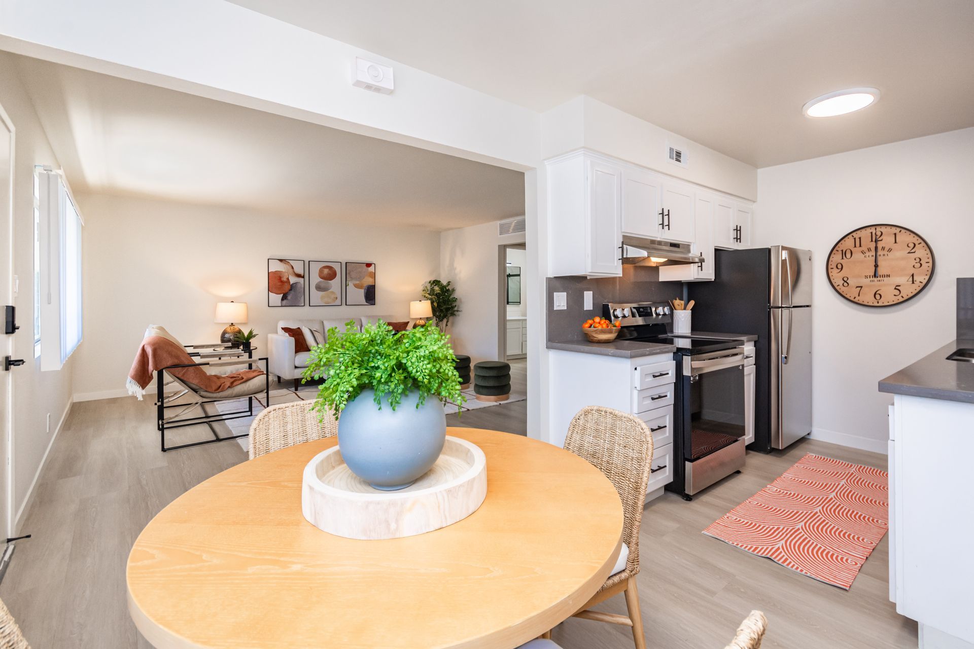 Bright kitchen and dining area with round table, blue vase centerpiece, and black appliances adjoining a living room.