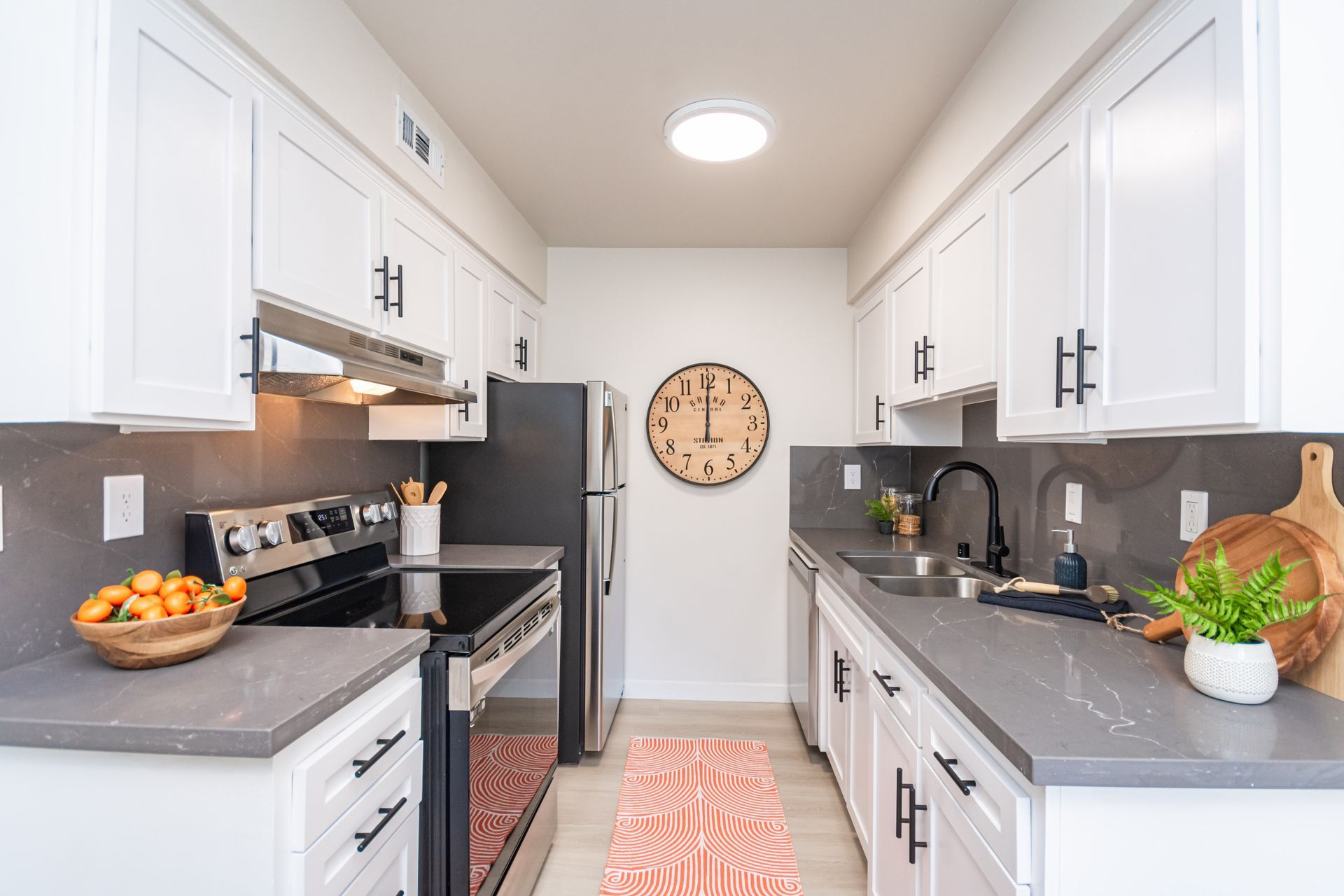 Bright white kitchen with gray countertops, stainless stove, wall clock, and fruit bowls on both counters