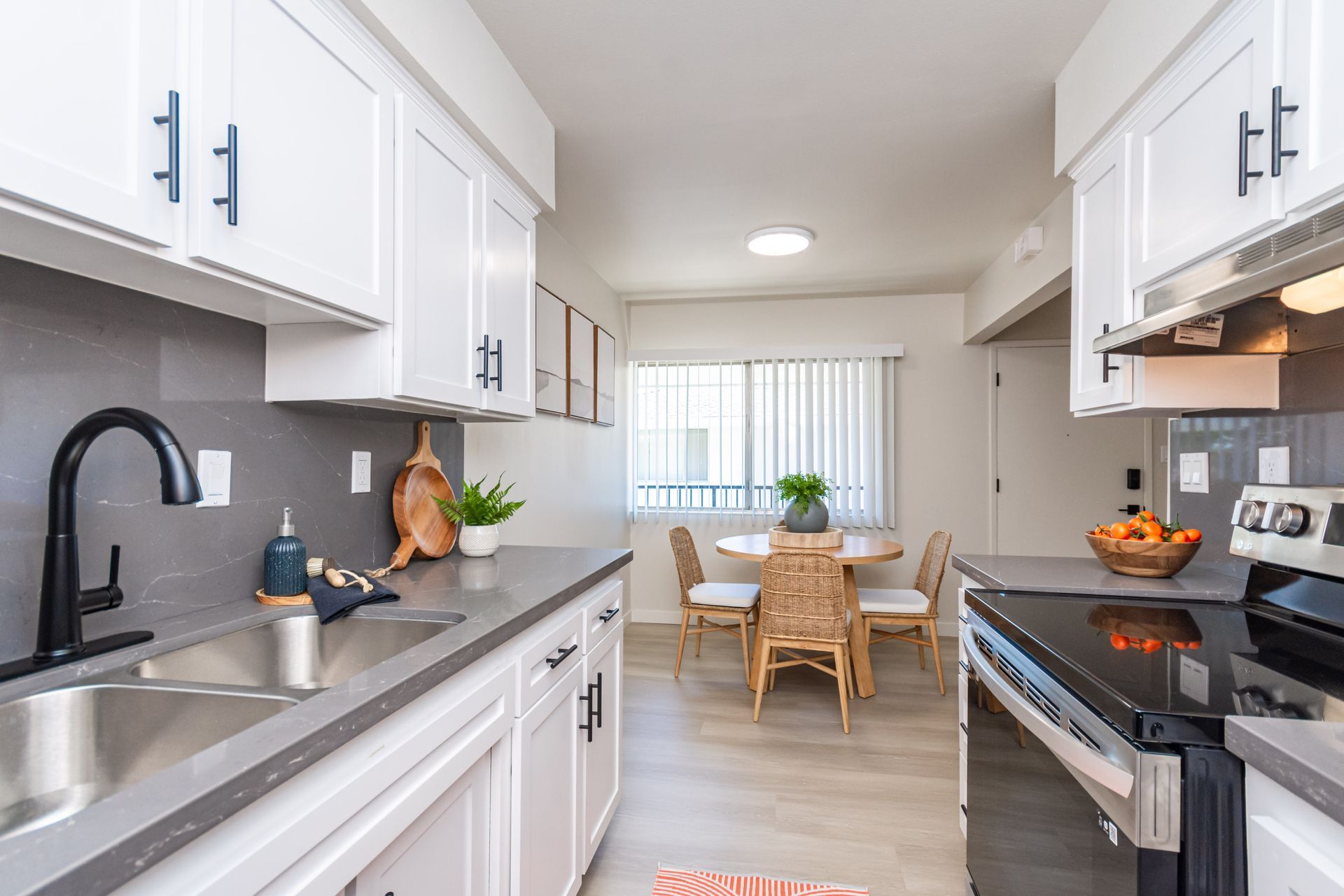 Bright white kitchen with black appliances, stainless sink, and a small dining area by a window