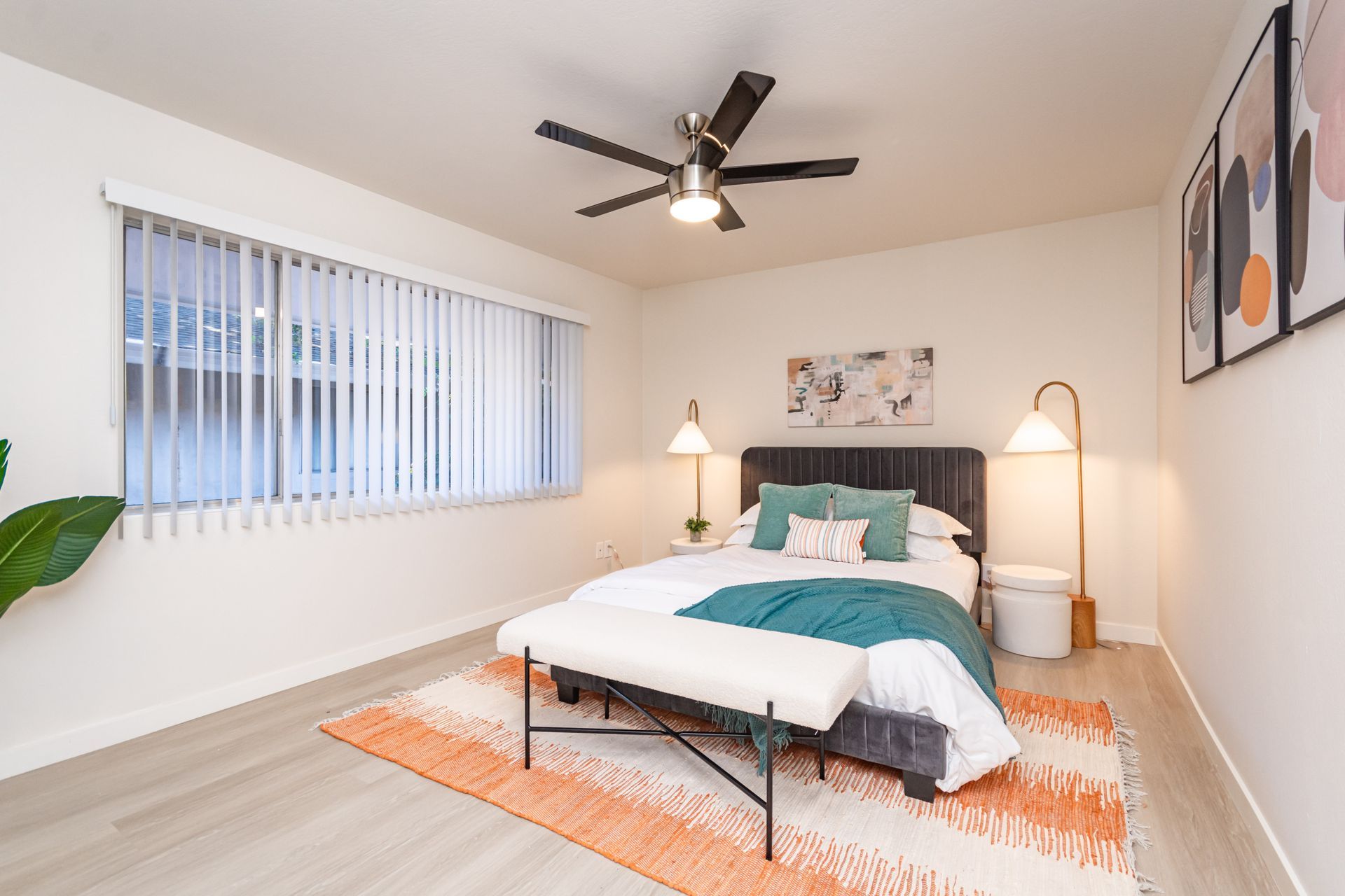 Bright bedroom with a bed, nightstands, lamps, orange rug, and ceiling fan.